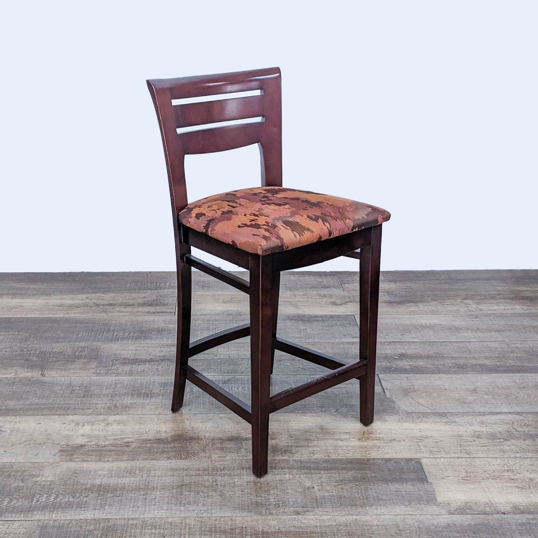 Reperch stool with a dark wood frame and a seat covered in a fabric with an earth-toned pattern, against a gray wood floor.