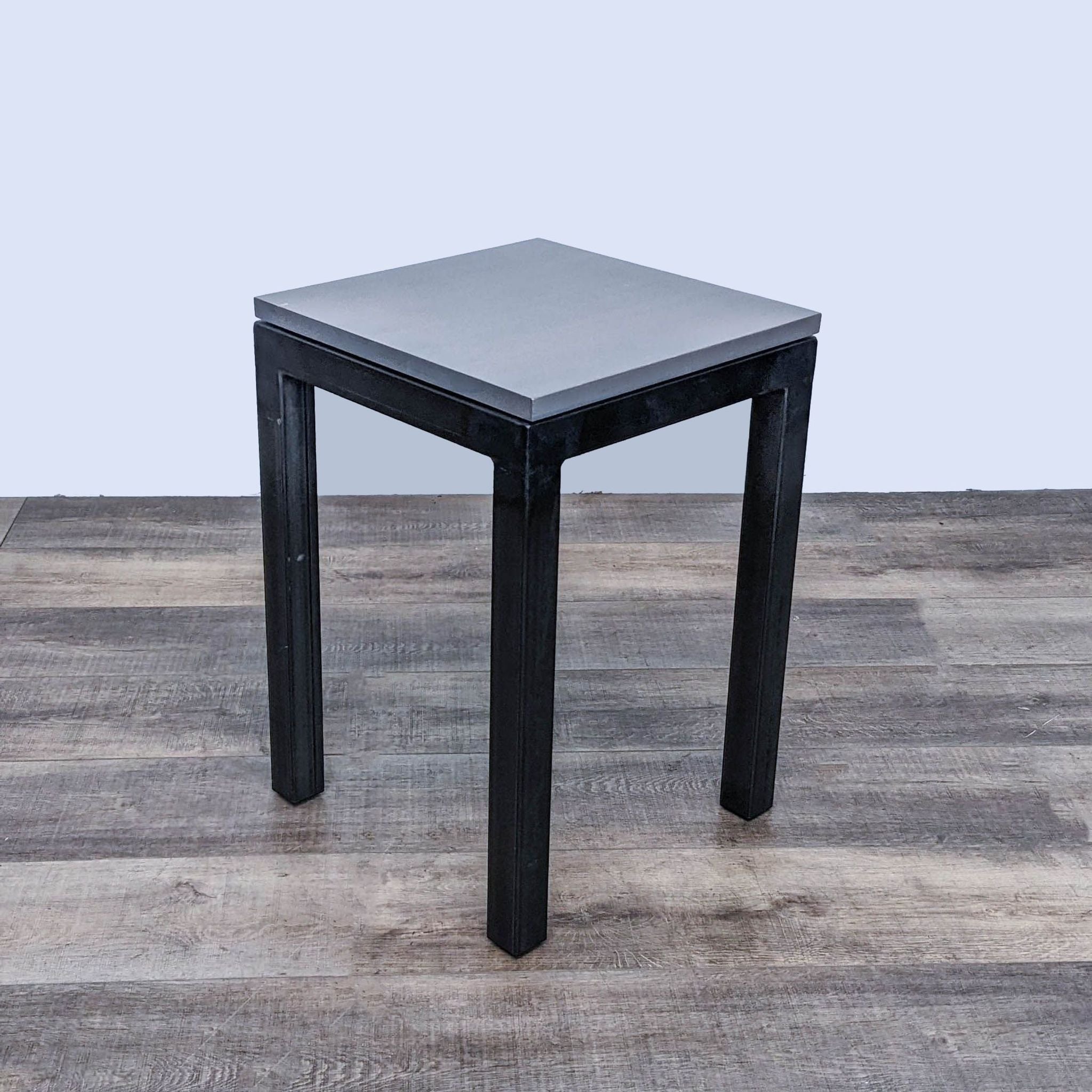 A sleek, modern console table by Room & Board with a metallic surface and dark legs, against a wooden background.