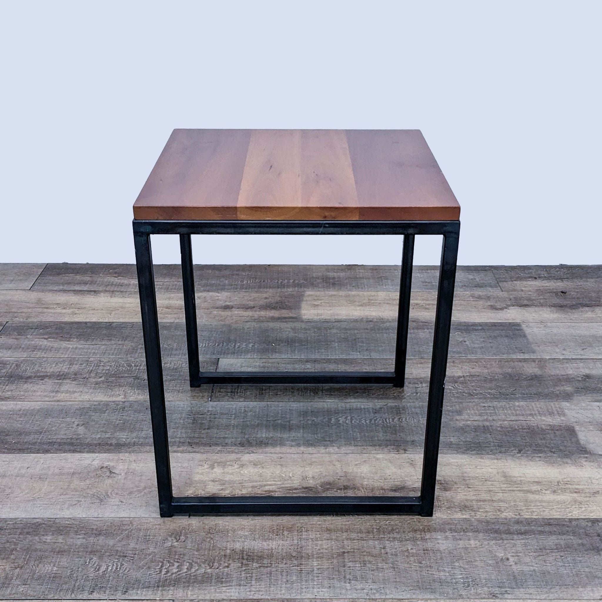 End table by Reperch featuring a geometric metal base and rectangular wooden surface, against a simple backdrop.