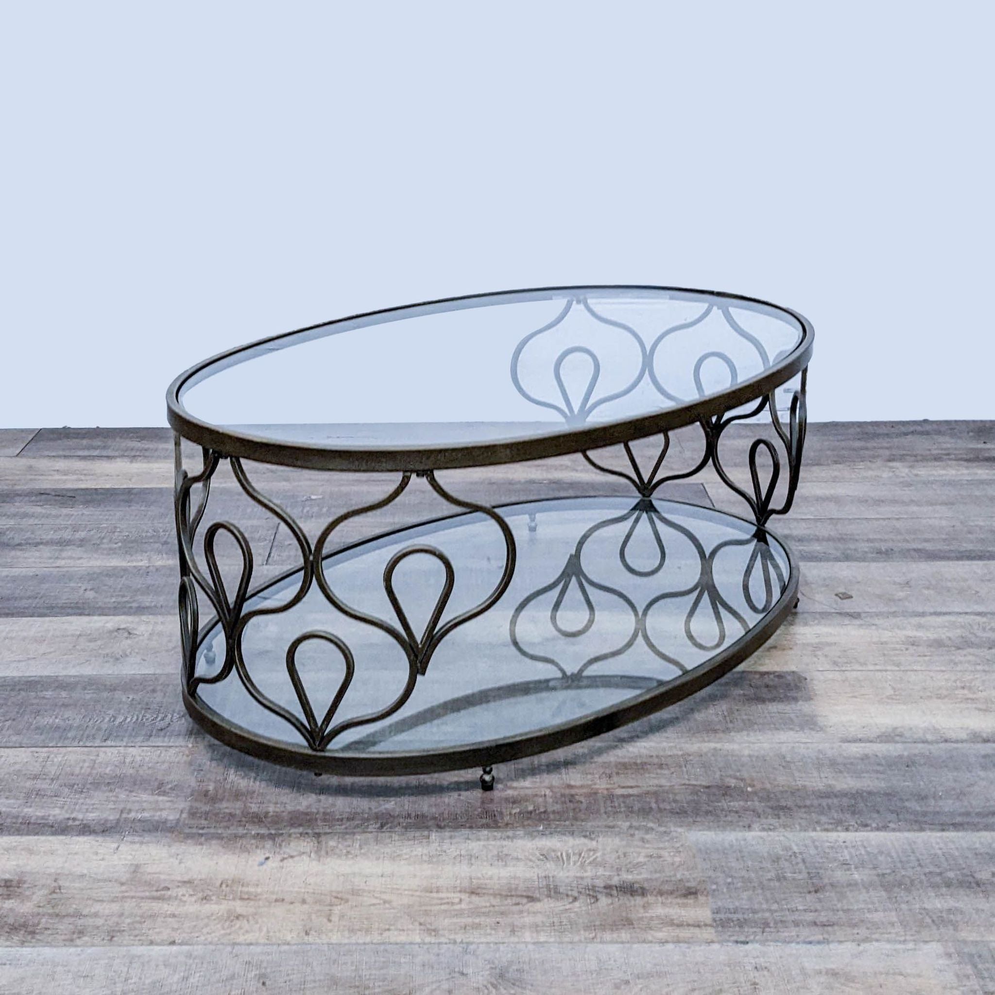 Reperch brand oval coffee table with glass top and decorative metal frame on wooden floor.