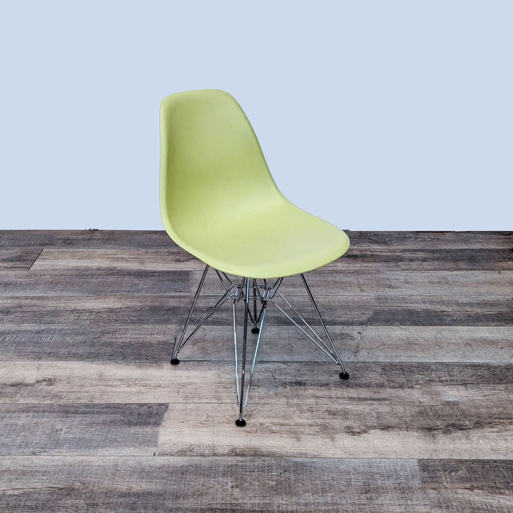 Vitra Eames dining chair with lime green molded plastic seat and chrome Eiffel wire base on wooden flooring.