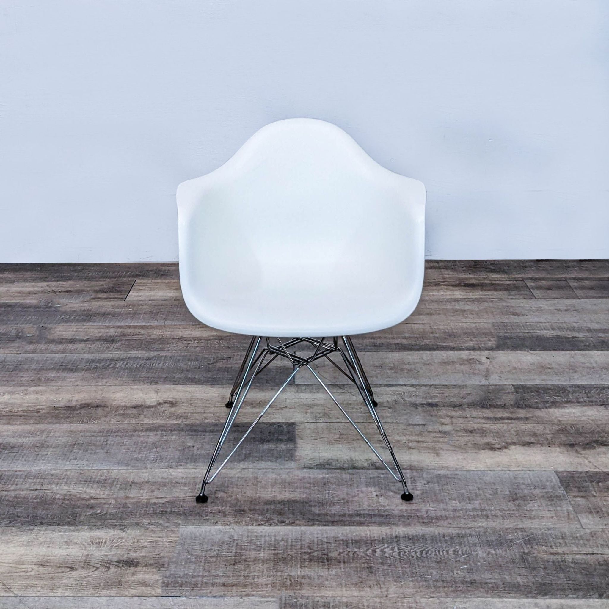 Herman Miller Eames armchair with white plastic seat and chrome Eiffel base on wood floor, facing forward.