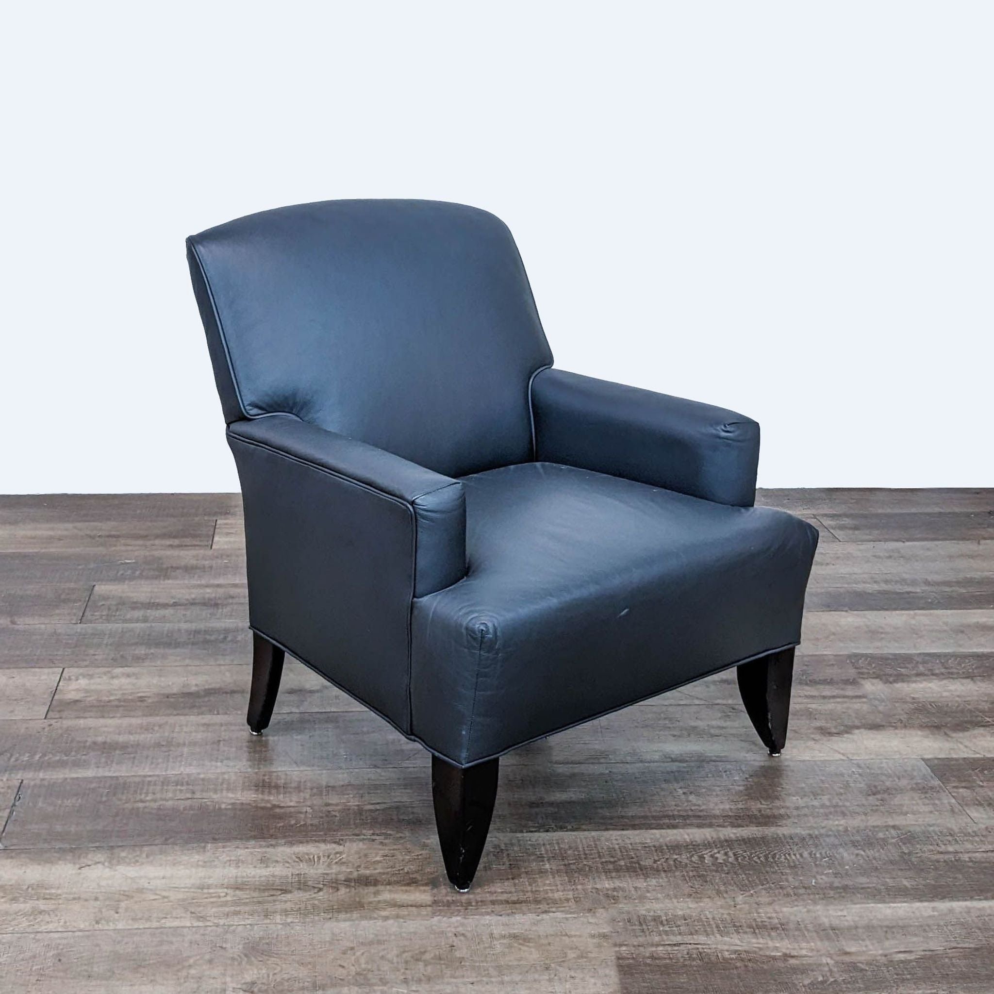 Reperch brand navy leather club chair with arched back and tapered wooden feet on a wood floor.