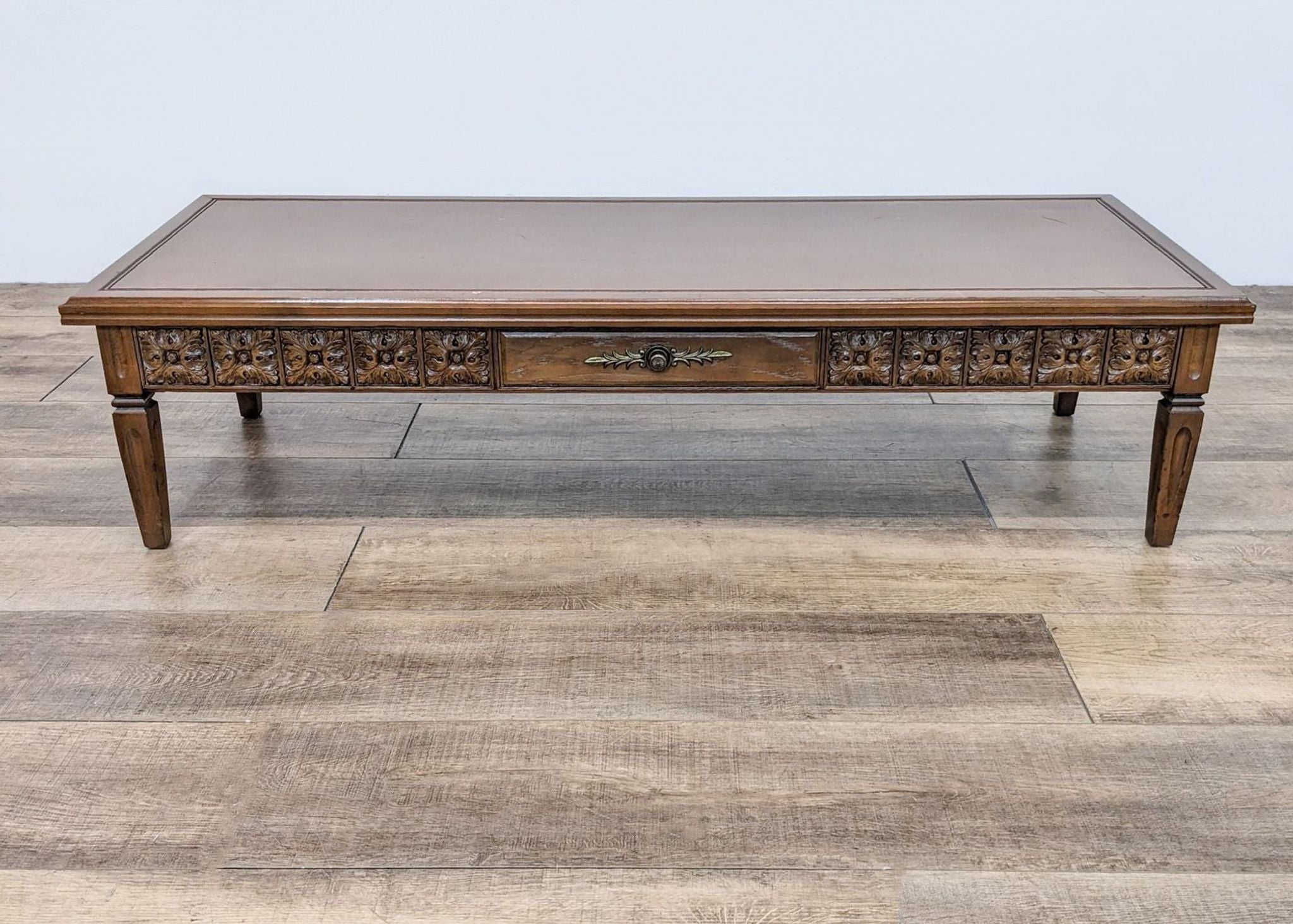 Wooden Reperch coffee table featuring decorative metal backplate on faux drawer amidst carved floral details.