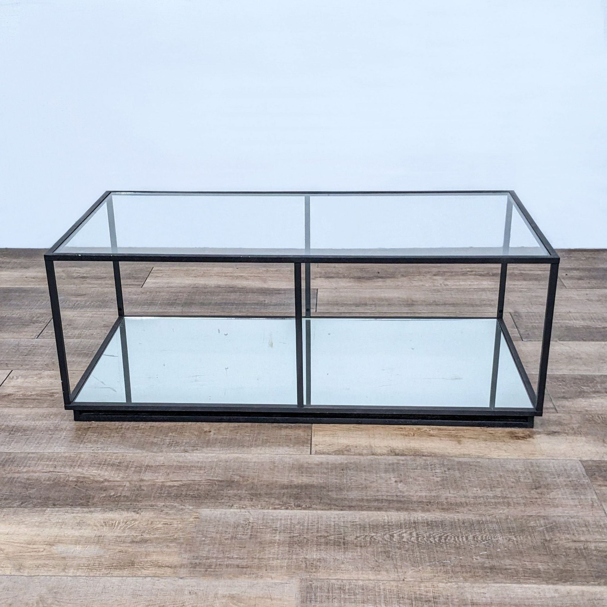 Sleek Reperch coffee table with metallic frame and clear glass surfaces, against a wood-patterned backdrop.