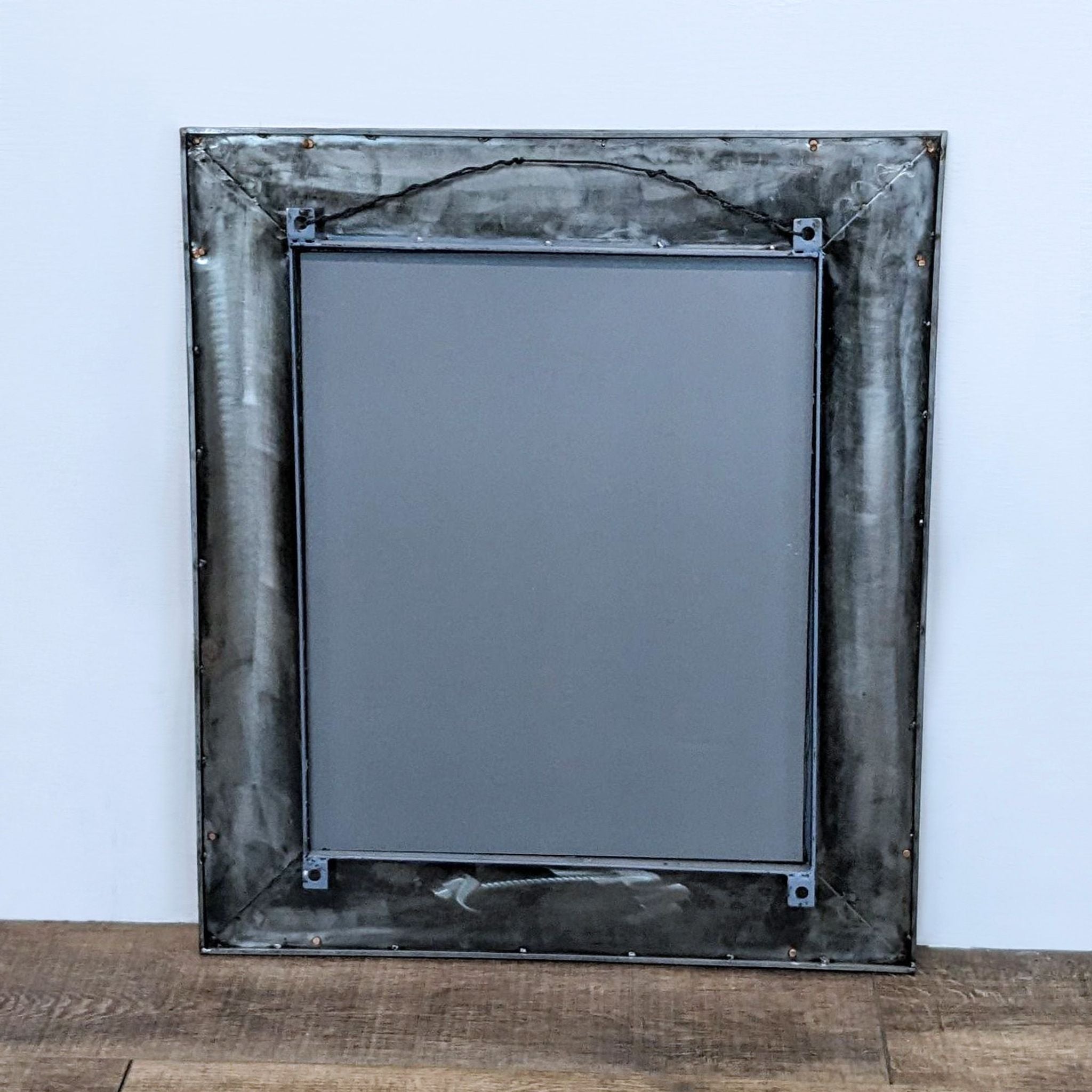 Rear view of a Reperch metal wall mirror, showing the frame's construction and hanging mechanism against a wooden floor and white wall.
