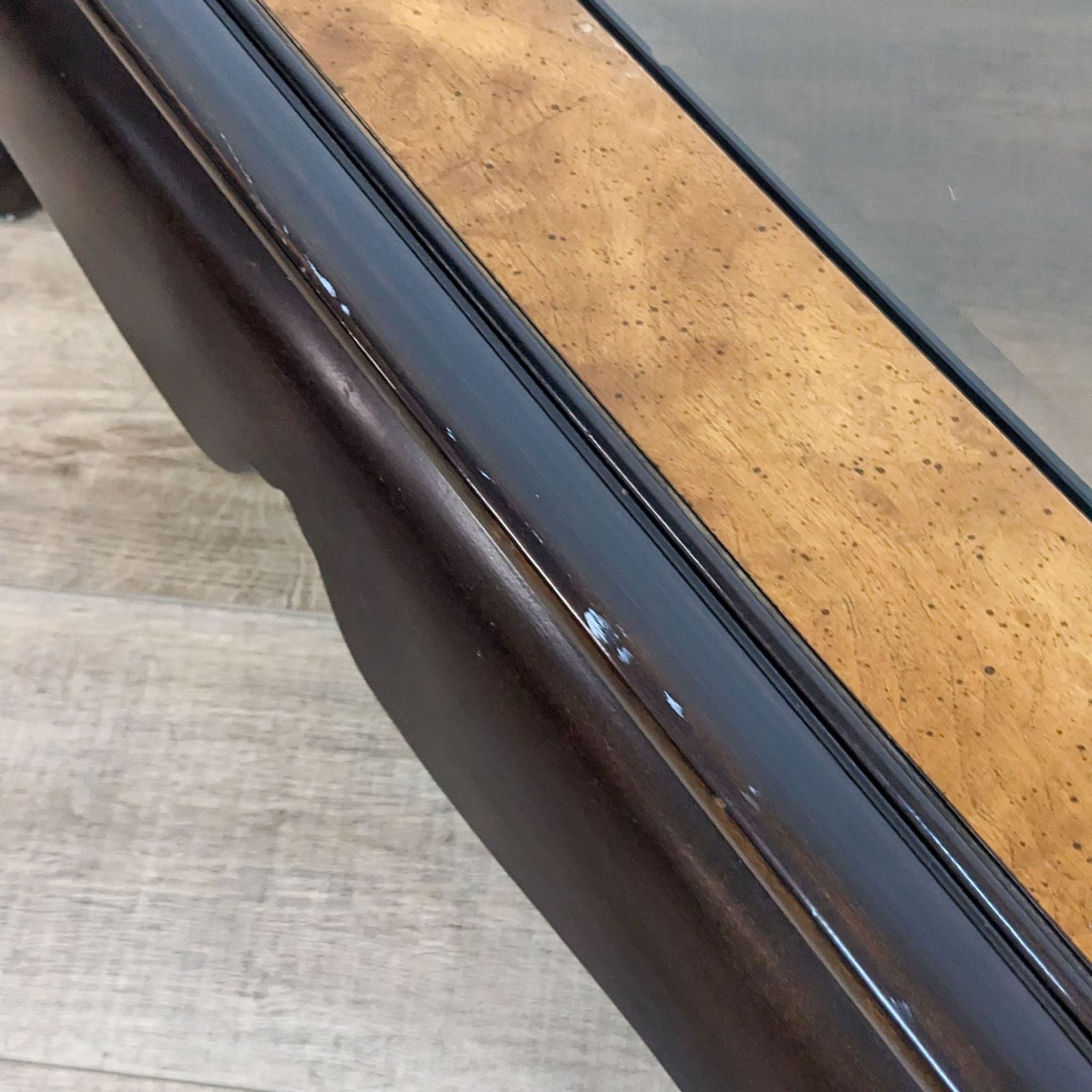 Close-up of a Reperch coffee table's burlwood frame and glass top edge.