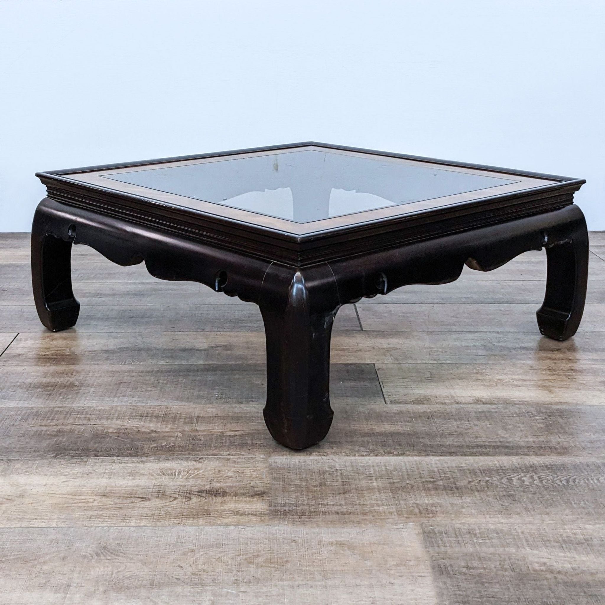 Elegant Reperch burlwood framed coffee table featuring a clear glass top and sturdy legs, positioned on a textured floor.