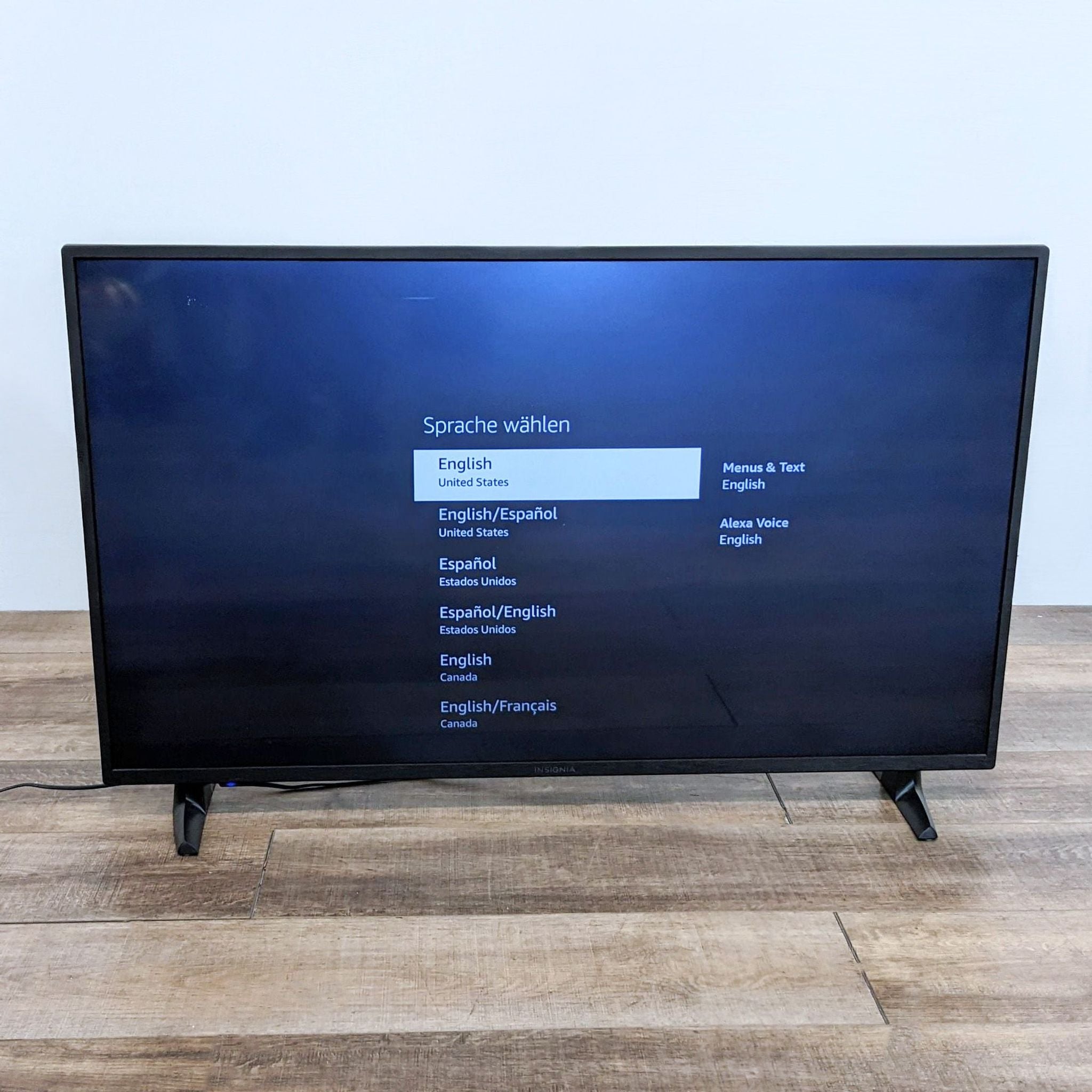 Insignia 4K UHD Fire TV displaying language selection menu with English highlighted, on a wood floor.