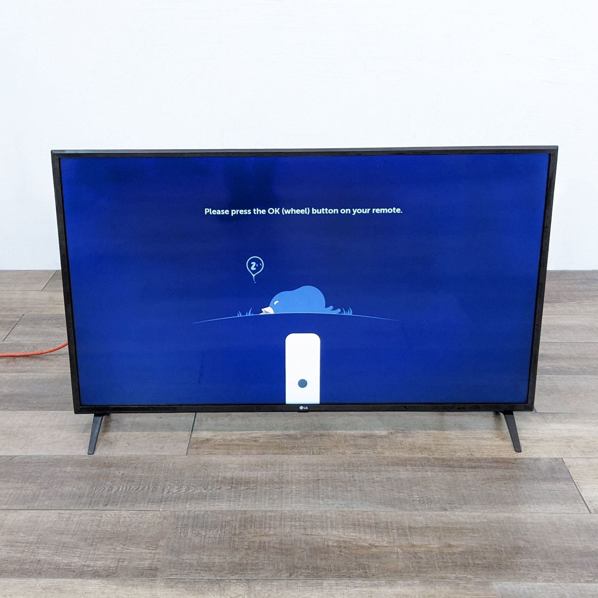 LG television on wooden floor displaying setup screen with a remote control prompt.