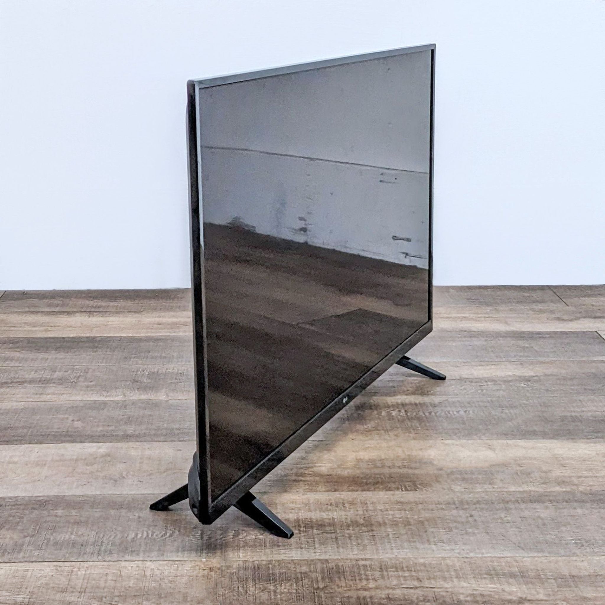 An LG TV on a stand displaying a clear reflective screen on a wooden floor against a white wall.
