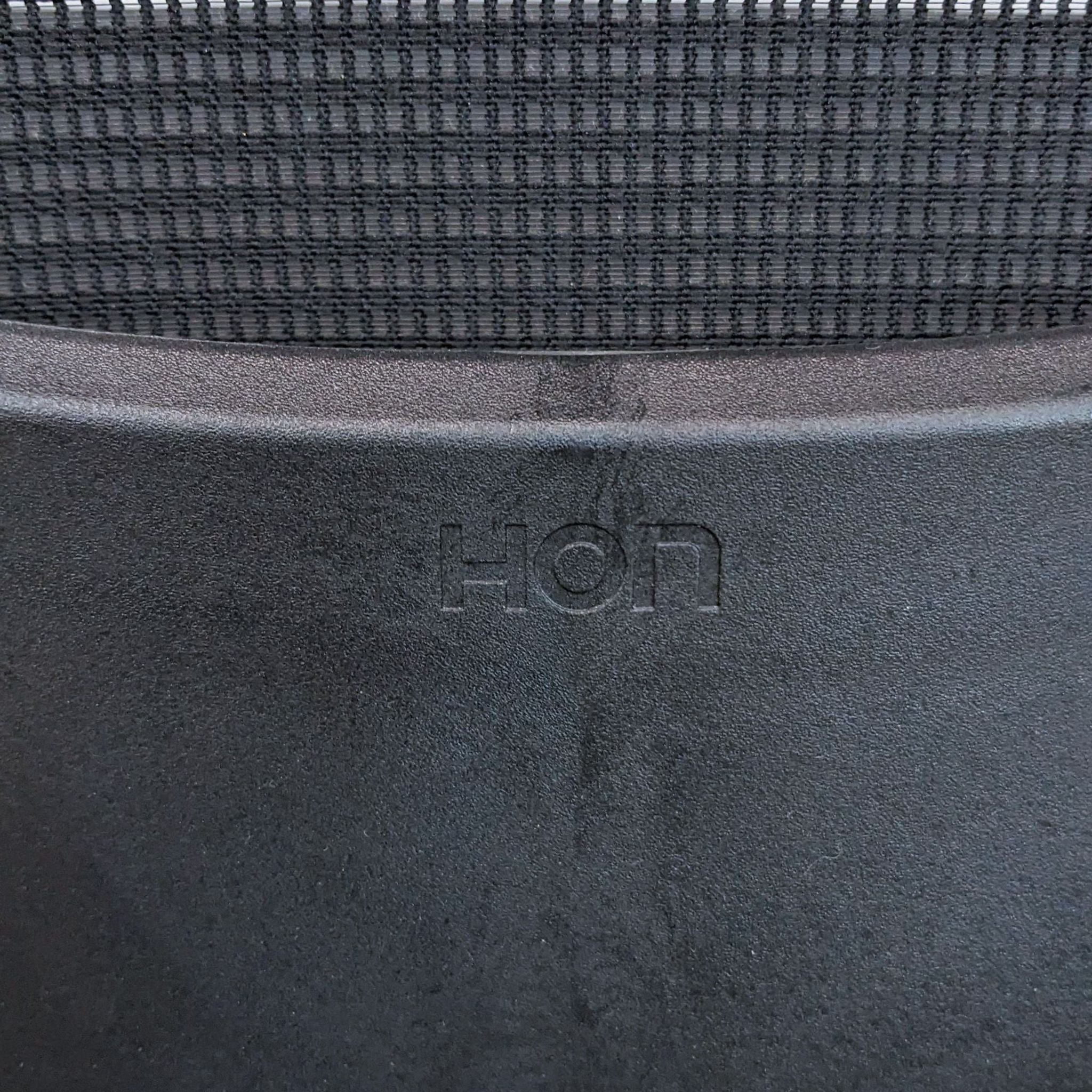 Close-up of HON logo on a modern barstool with stretch mesh back and durable steel frame.