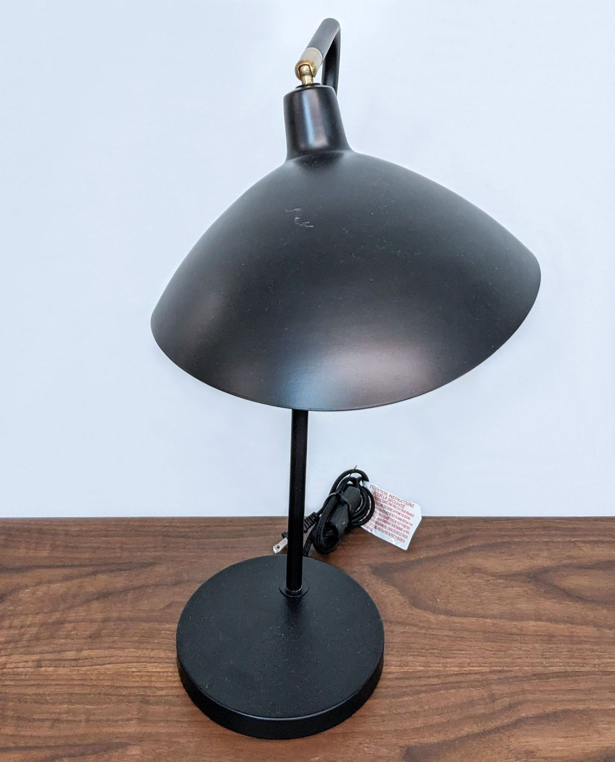 A black Safavieh table lamp featuring a golden interior, adjustable angle, placed on a brown surface with white backdrop.