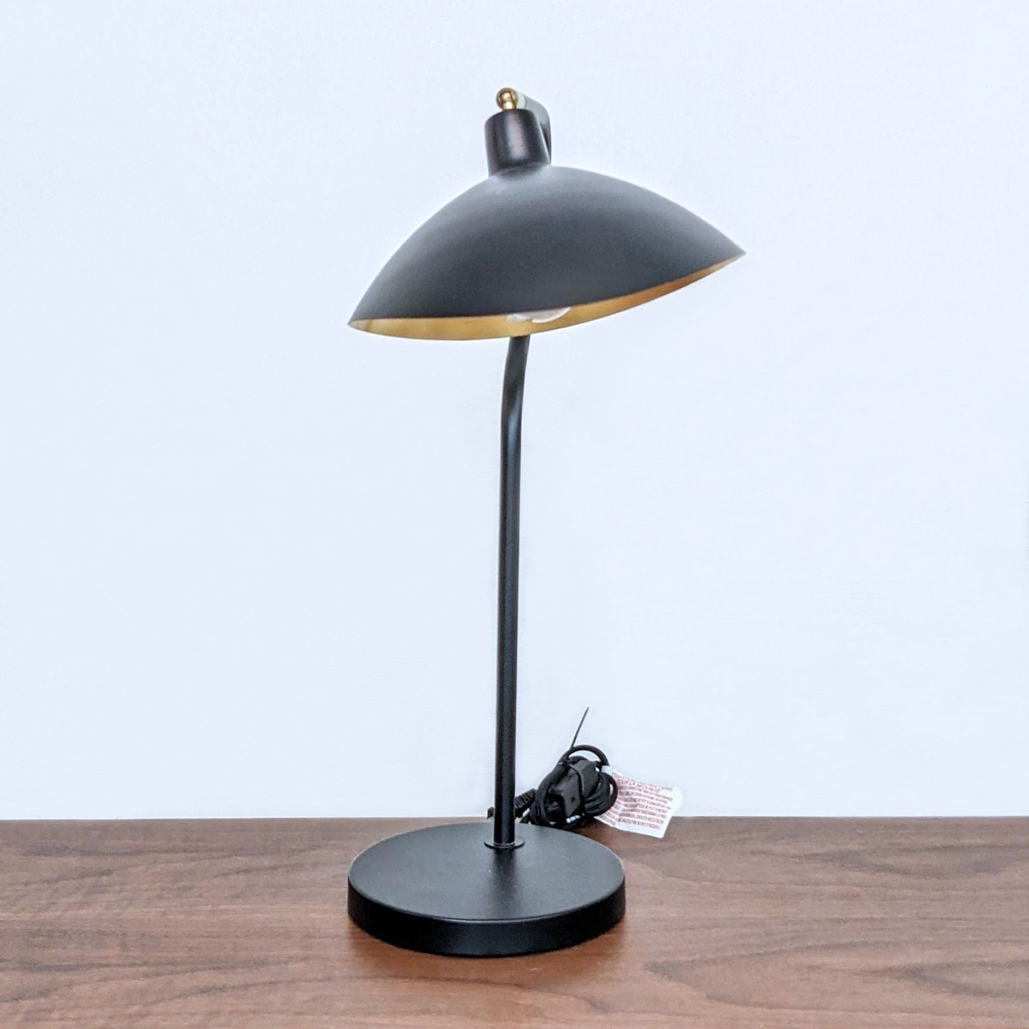 Safavieh black and gold desk lamp with a dome-shaped shade on a wooden table.