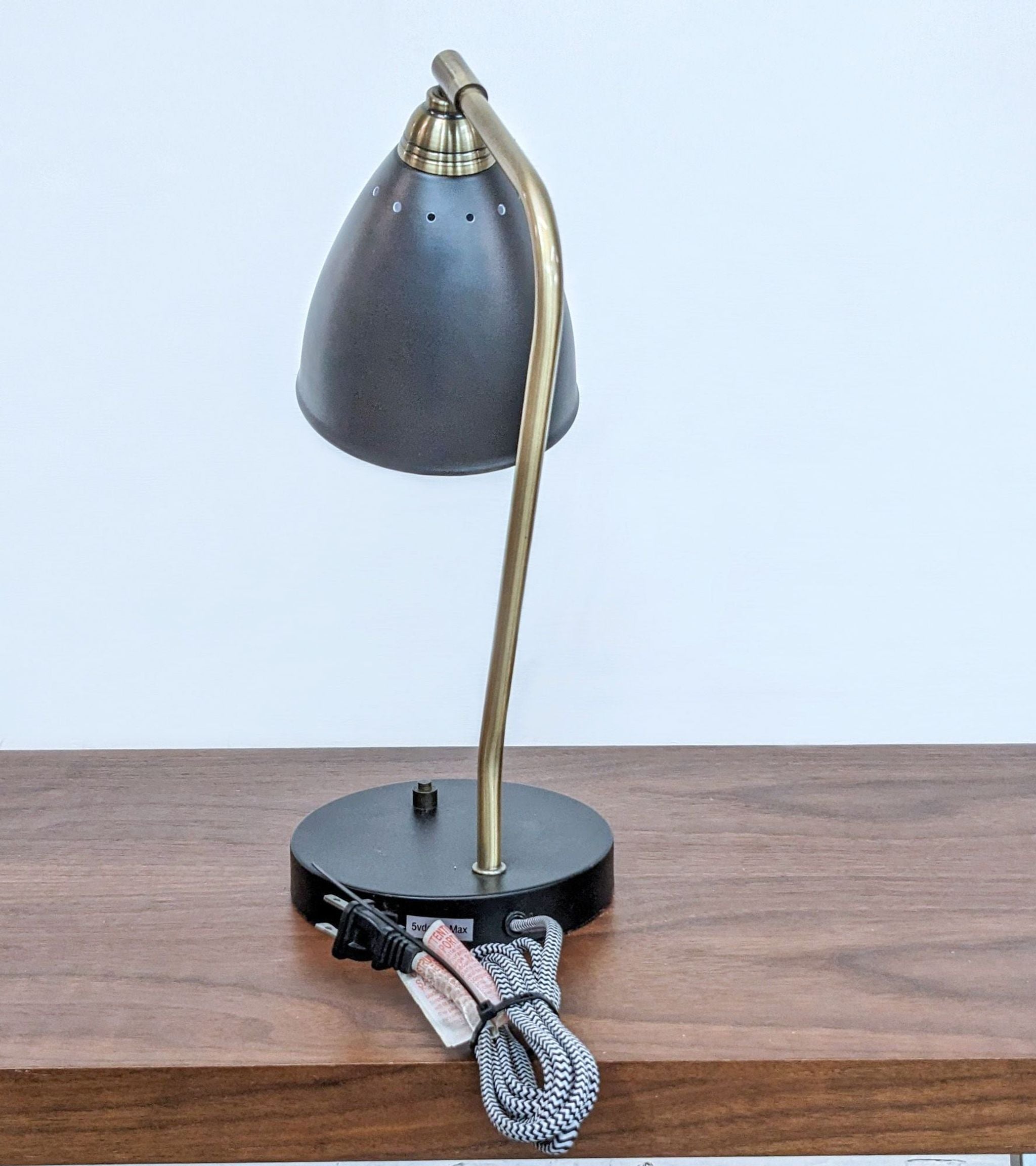 Arcadia Collection elegant desk lamp with a curved brass stand, dark grey shade, and black base with cord on a wooden table.