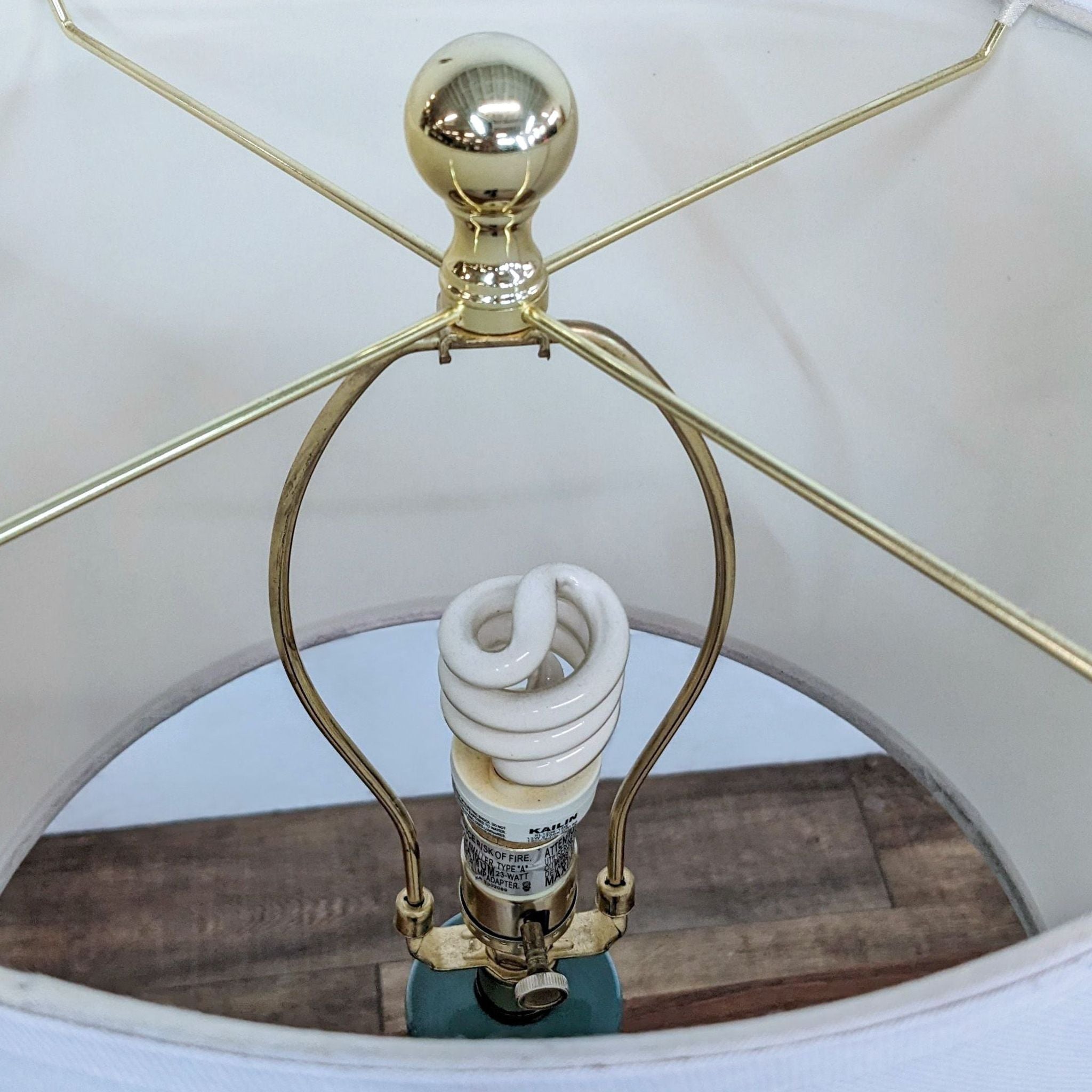 Safavieh branded lighting featuring a close-up of a CFL bulb and brass lamp structure with a spherical finial.