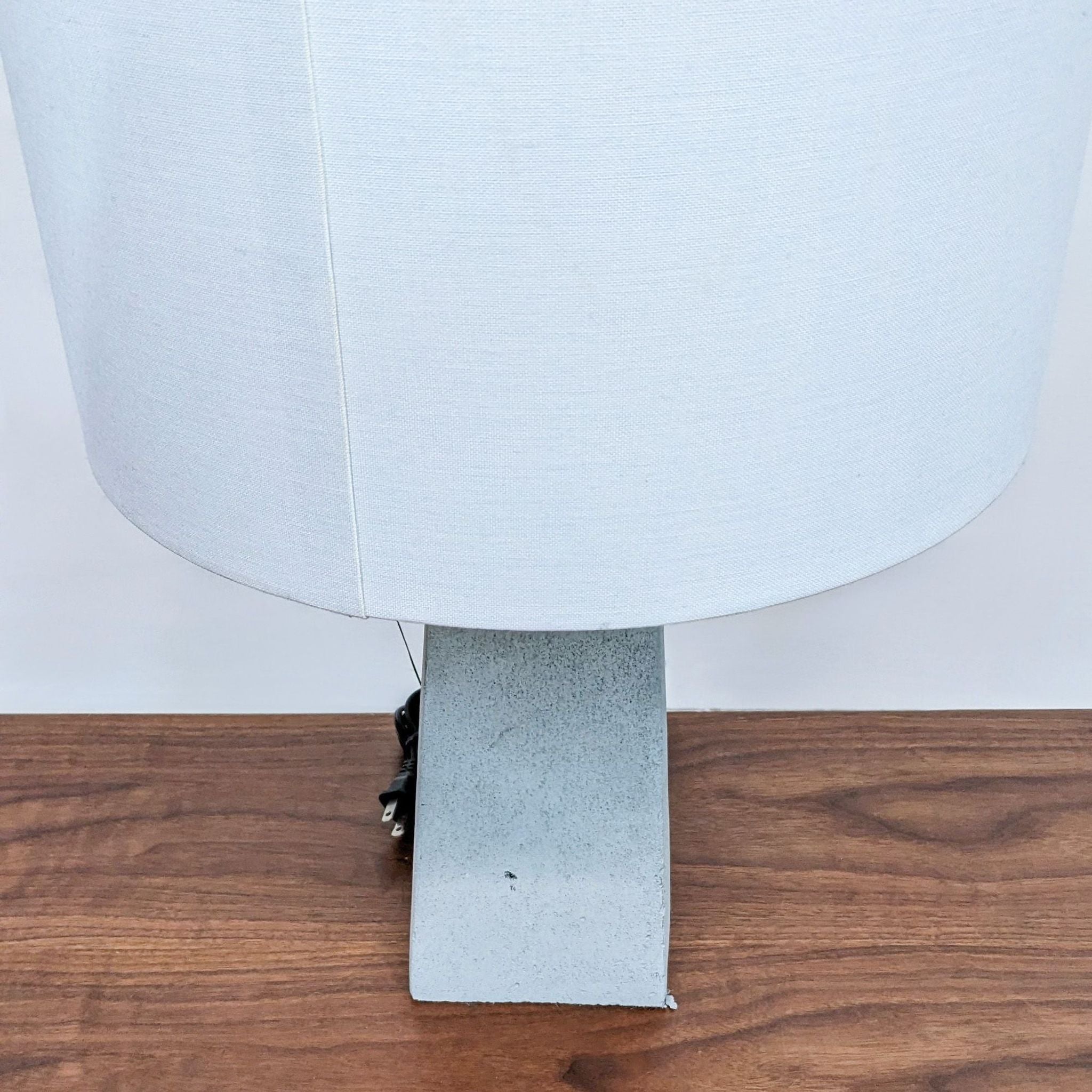 White fabric lampshade on a textured grey concrete base by Reperch, displayed on a wooden surface.