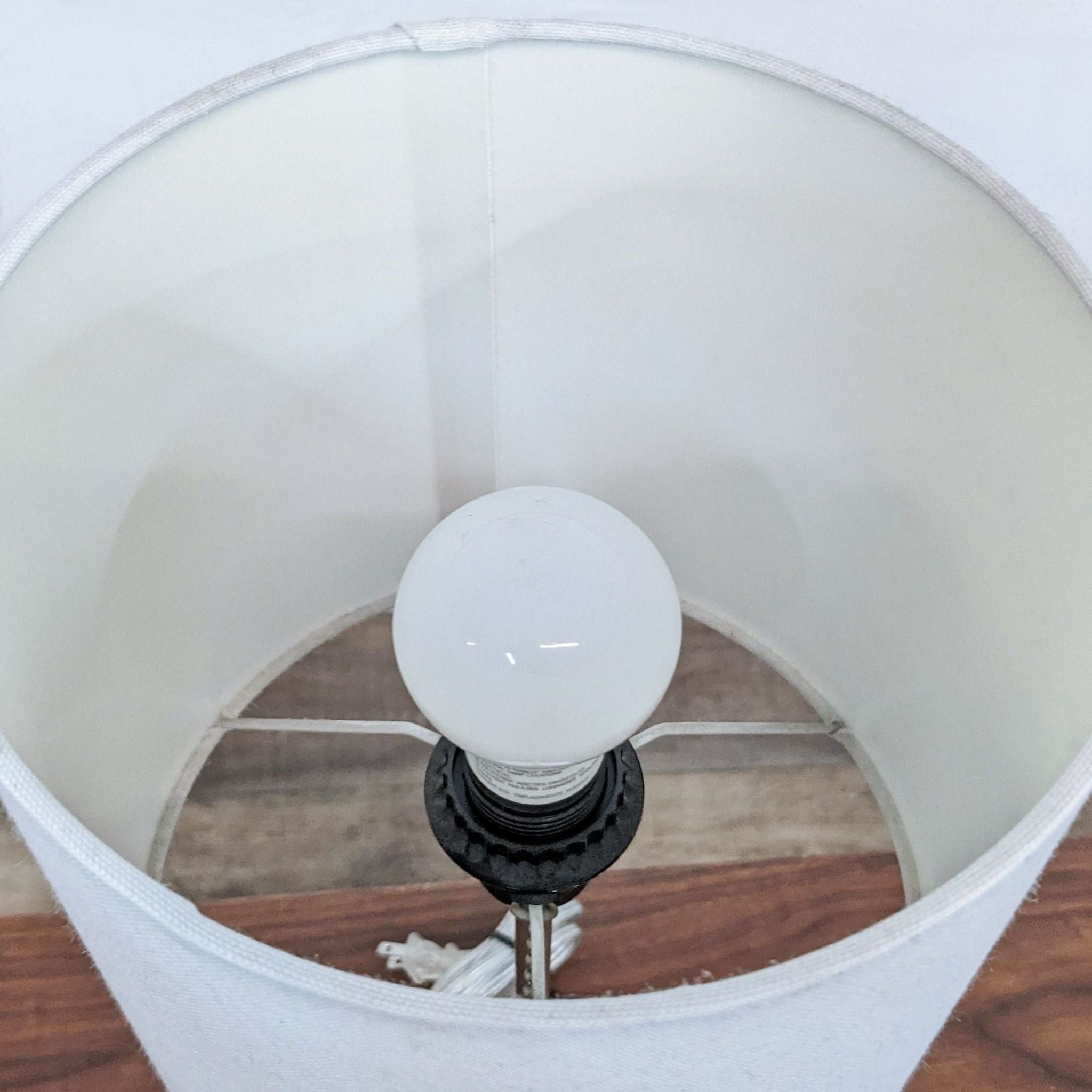 Alt text 2: Close-up view of a simple white Reperch lampshade and light bulb, revealing interior structure and details. Max length 100.