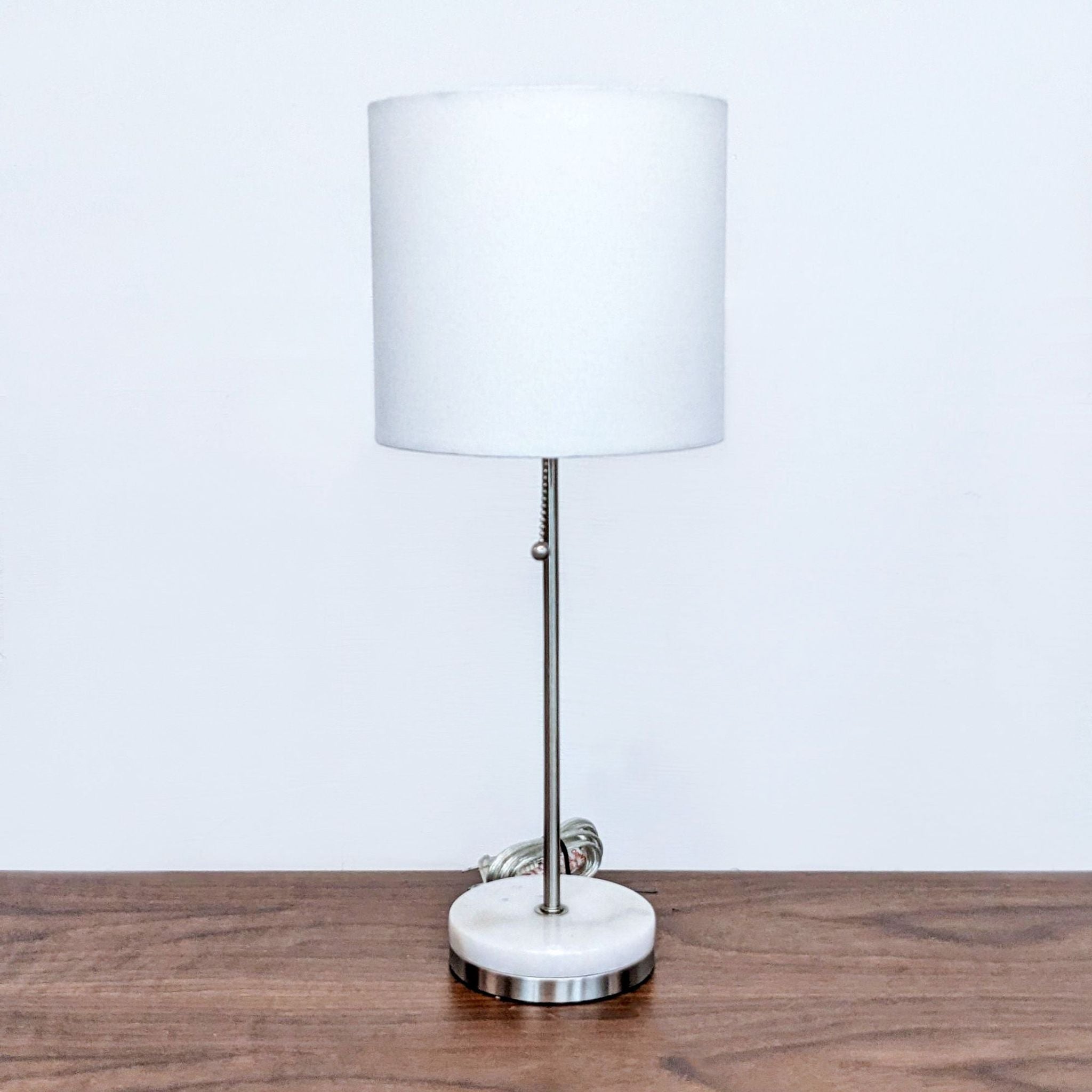Alt text 1: Modern Reperch table lamp with cylindrical white shade and silver base on wooden surface against white wall. Max length 100.