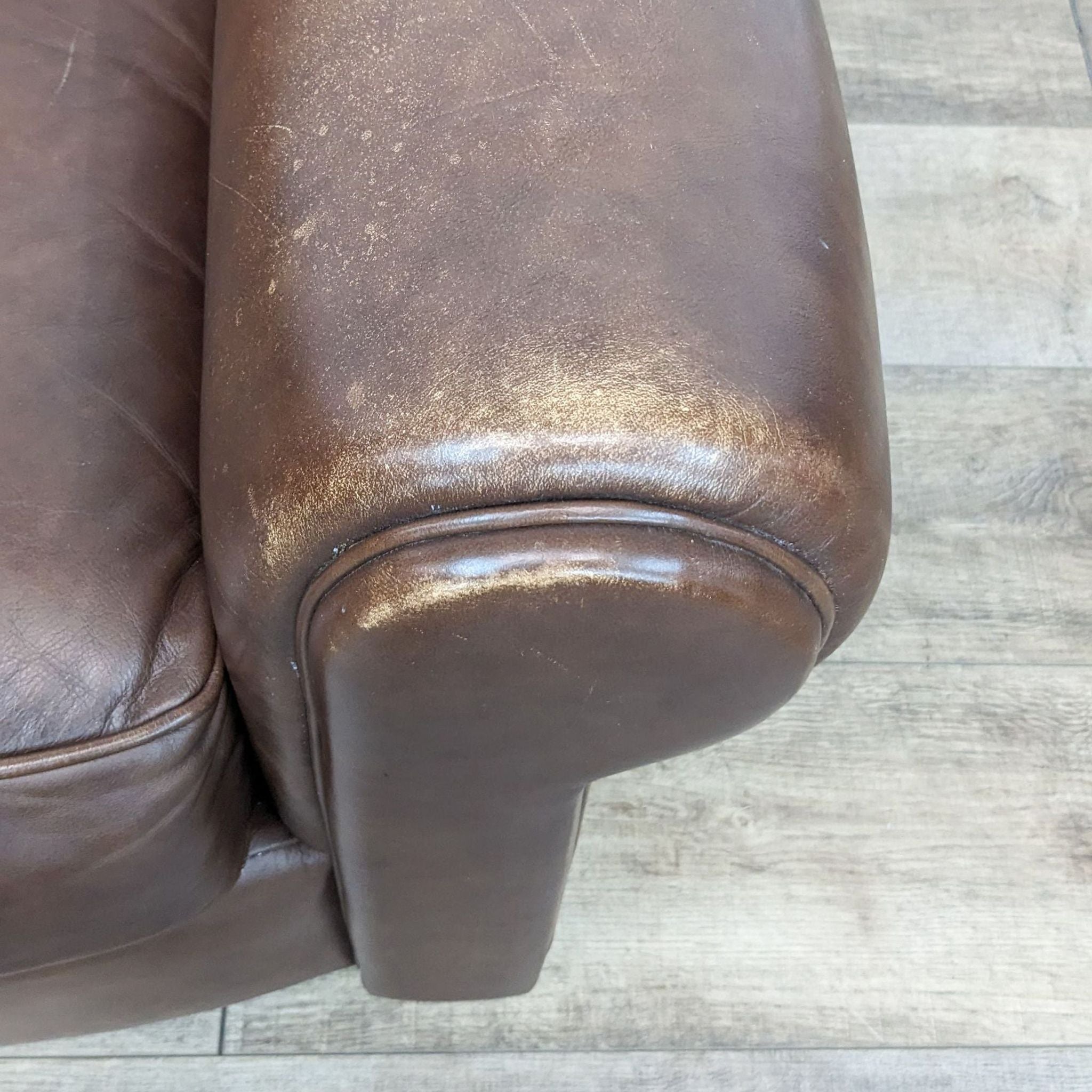 Close-up of Reperch contemporary leather club chair arm with rolled design and wood feet detail.