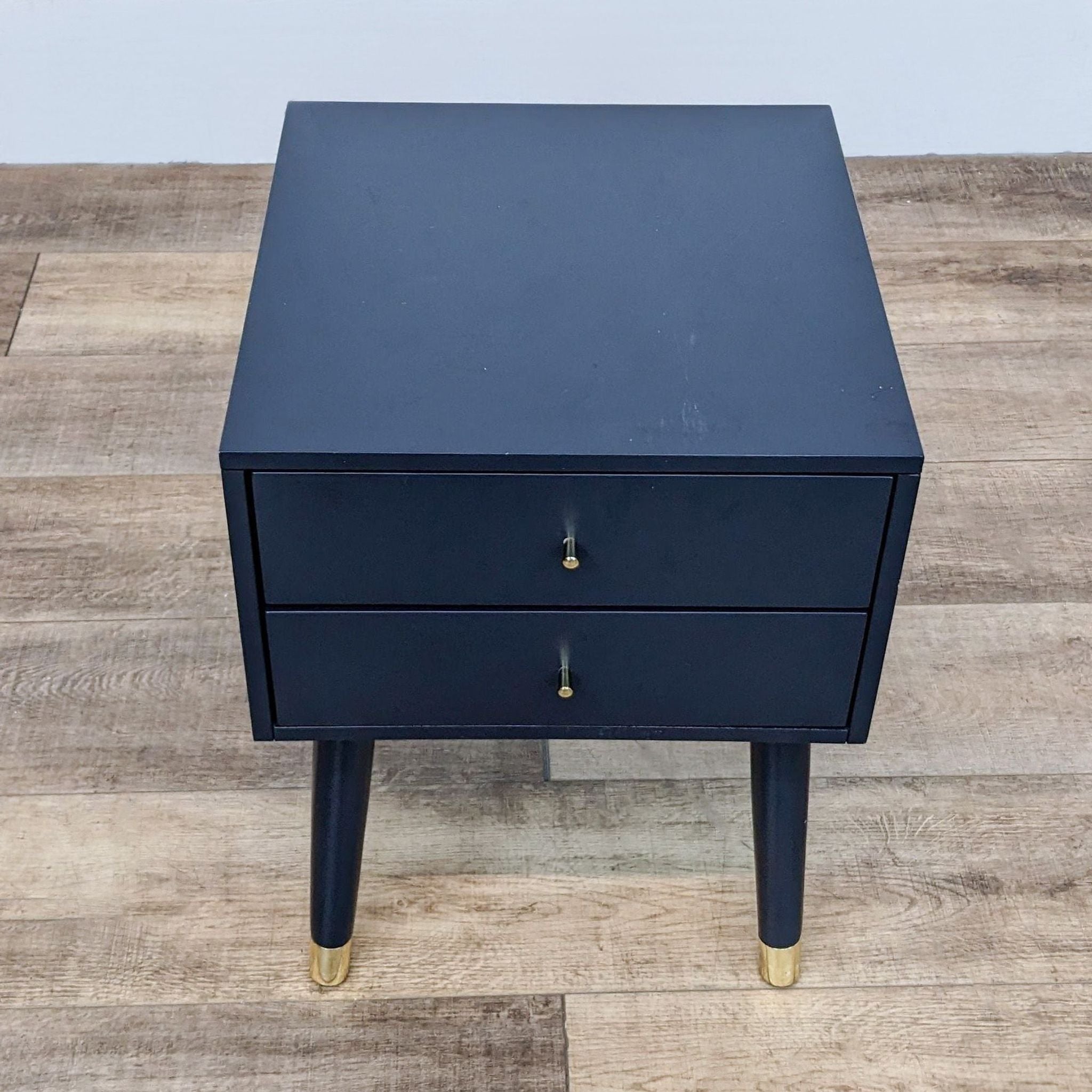 Safavieh end table with two drawers and angled legs with metallic caps on a wooden floor.