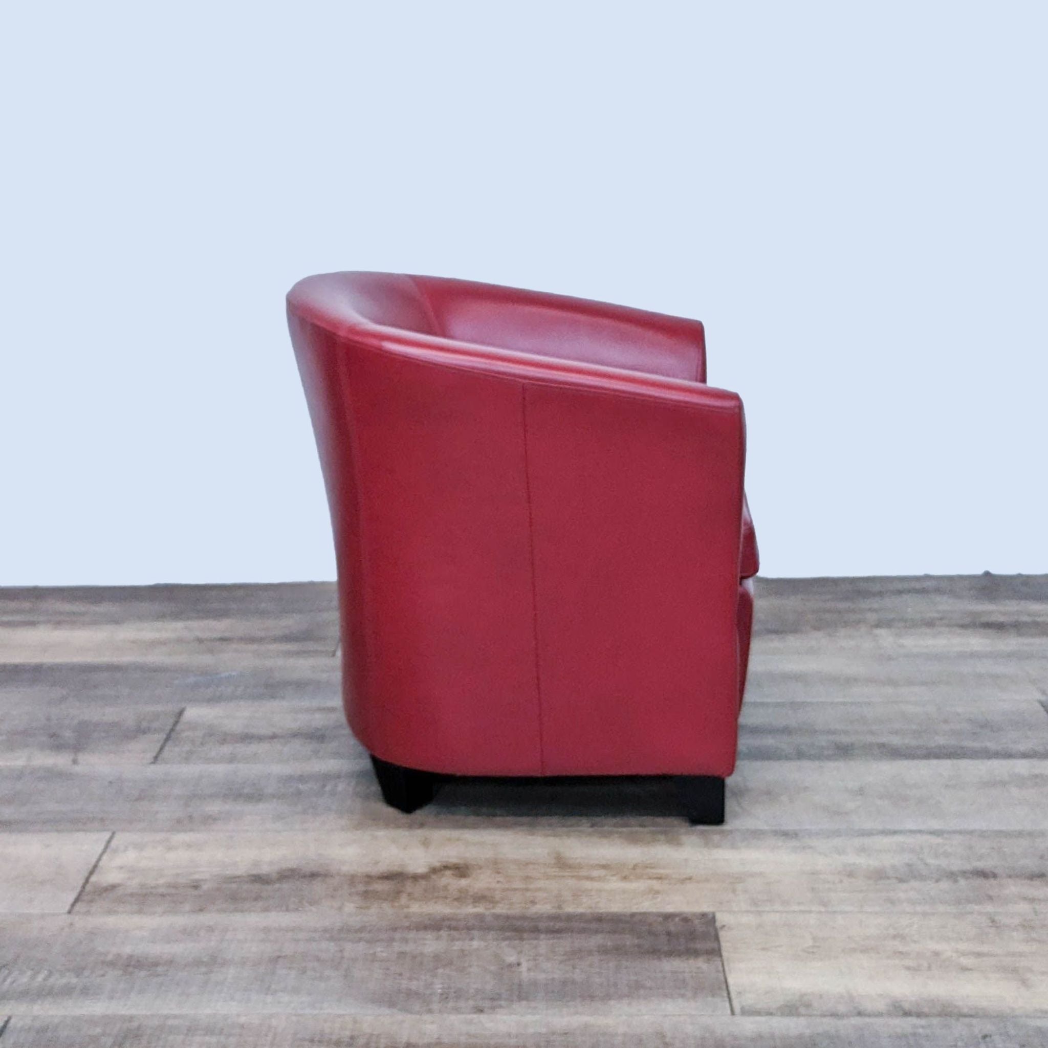 Art Deco red leather tub chair by Reperch, side angle, showcasing the chair's curved lines and wooden legs.