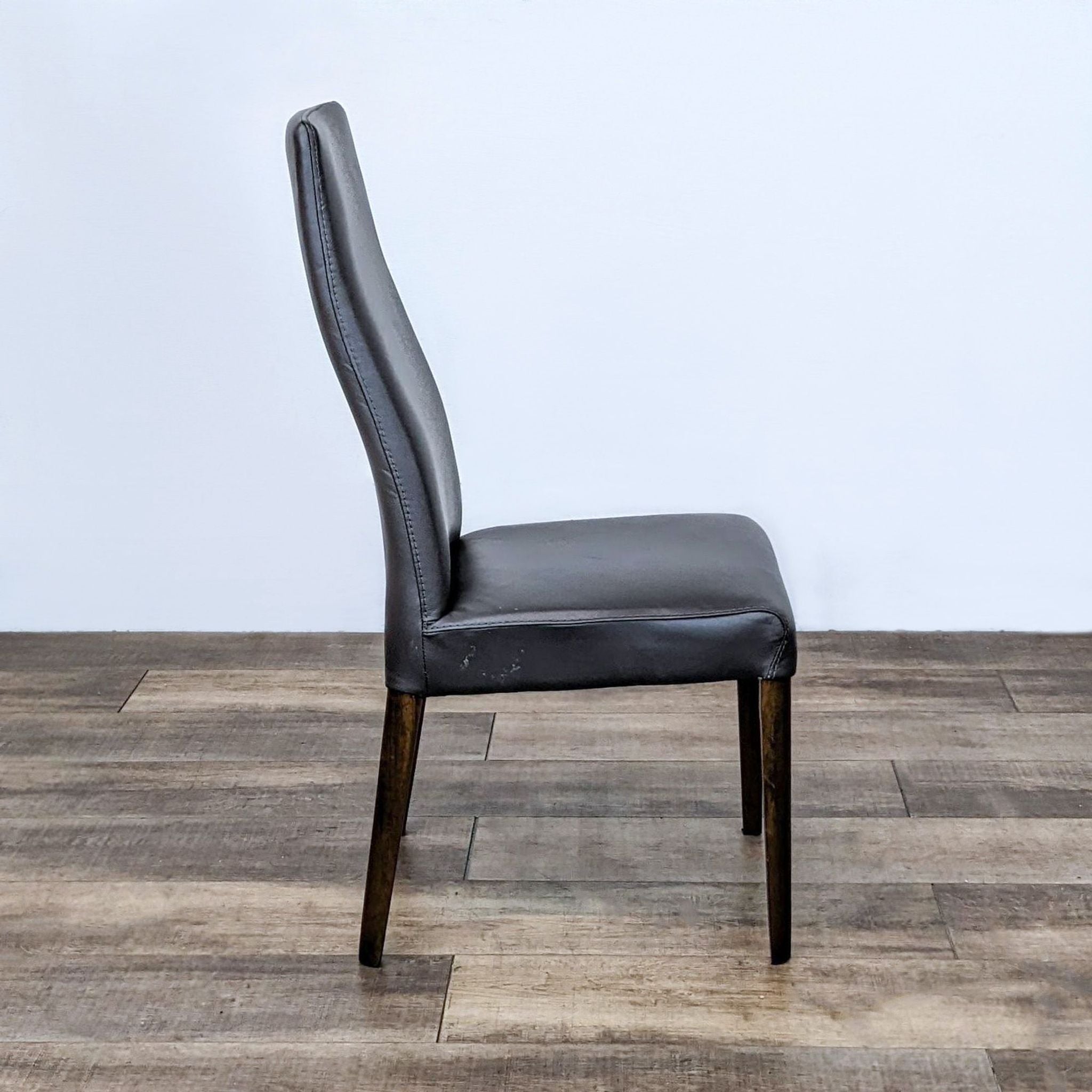 Side angle of a Reperch Scandinavian style leather upholstered dining chair with wooden legs.