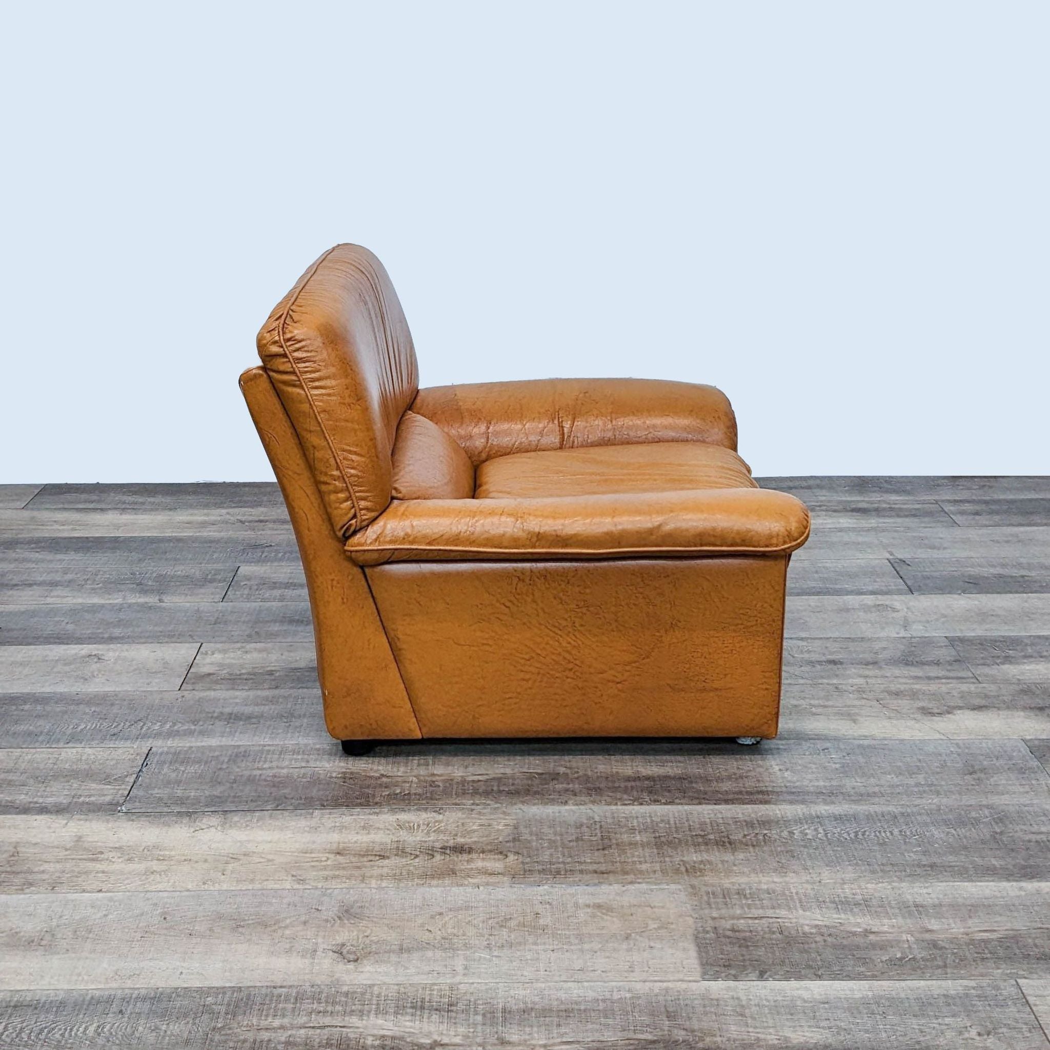 Contemporary Reperch lounge chair featuring a tan leather finish, comfortable padding, curved armrests, and wooden legs.