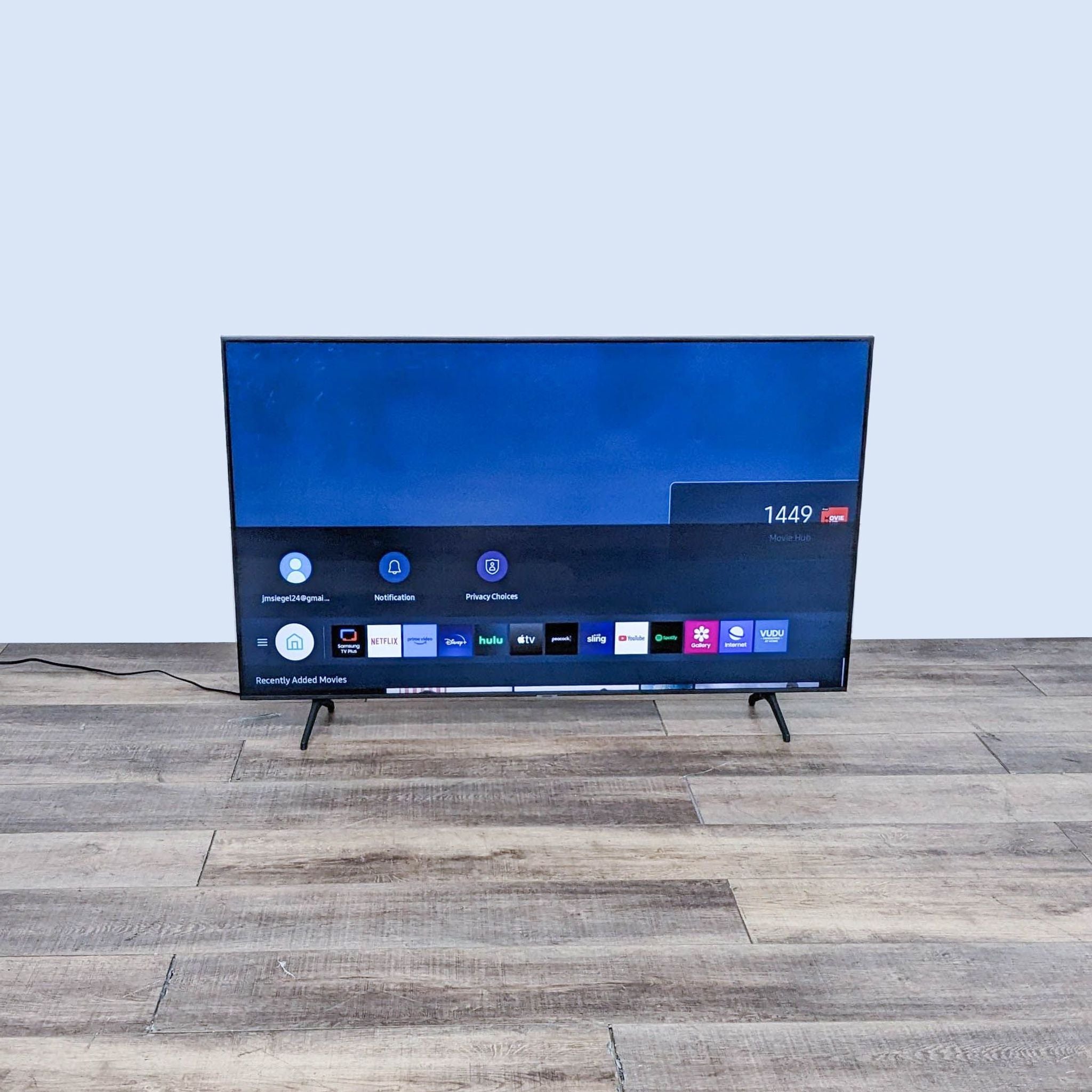 Samsung high-definition TV displaying a menu screen with app icons, set on a wood-textured surface.
