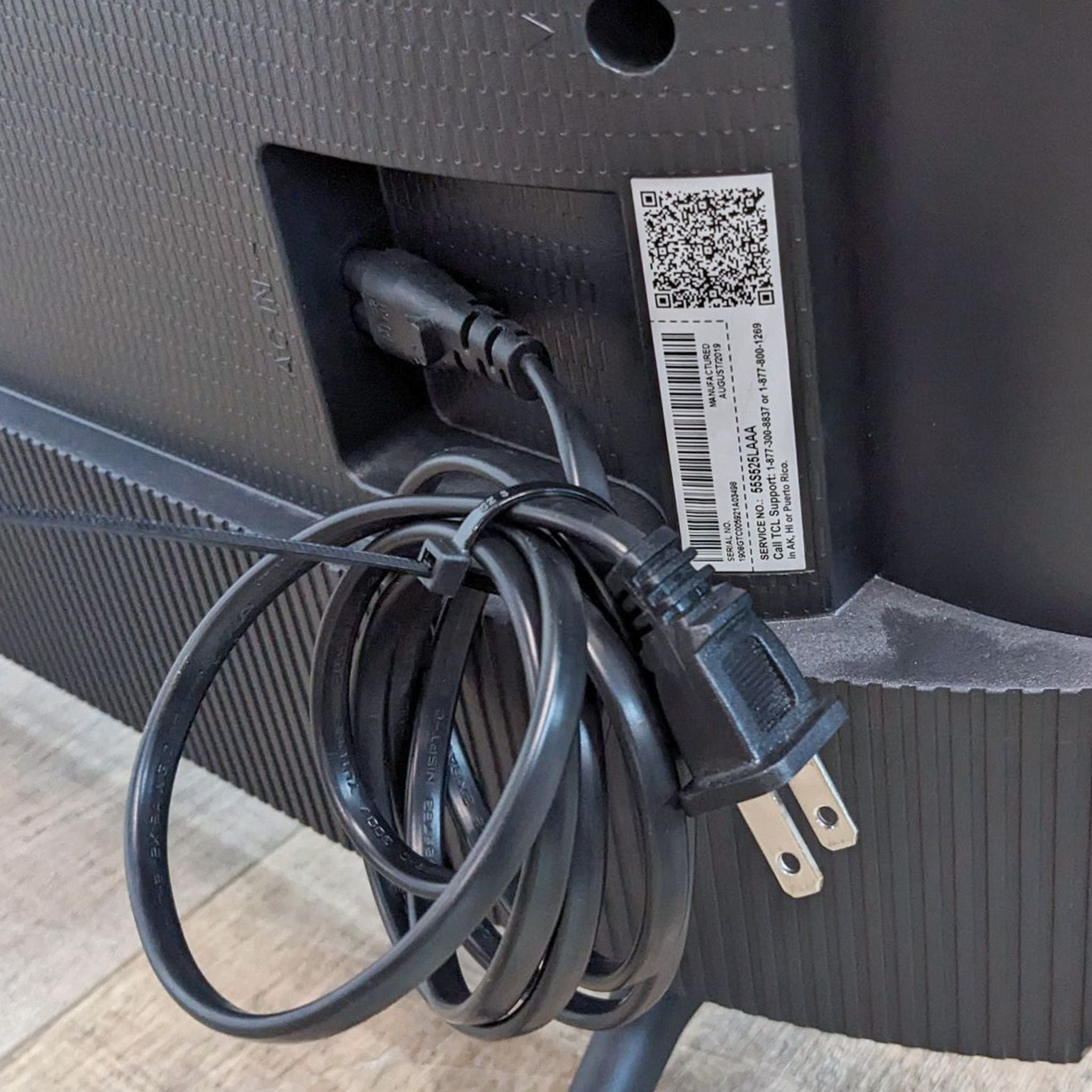 Power cable coiled at the back of a TCL 55S525 TV with QR code and serial number visible.