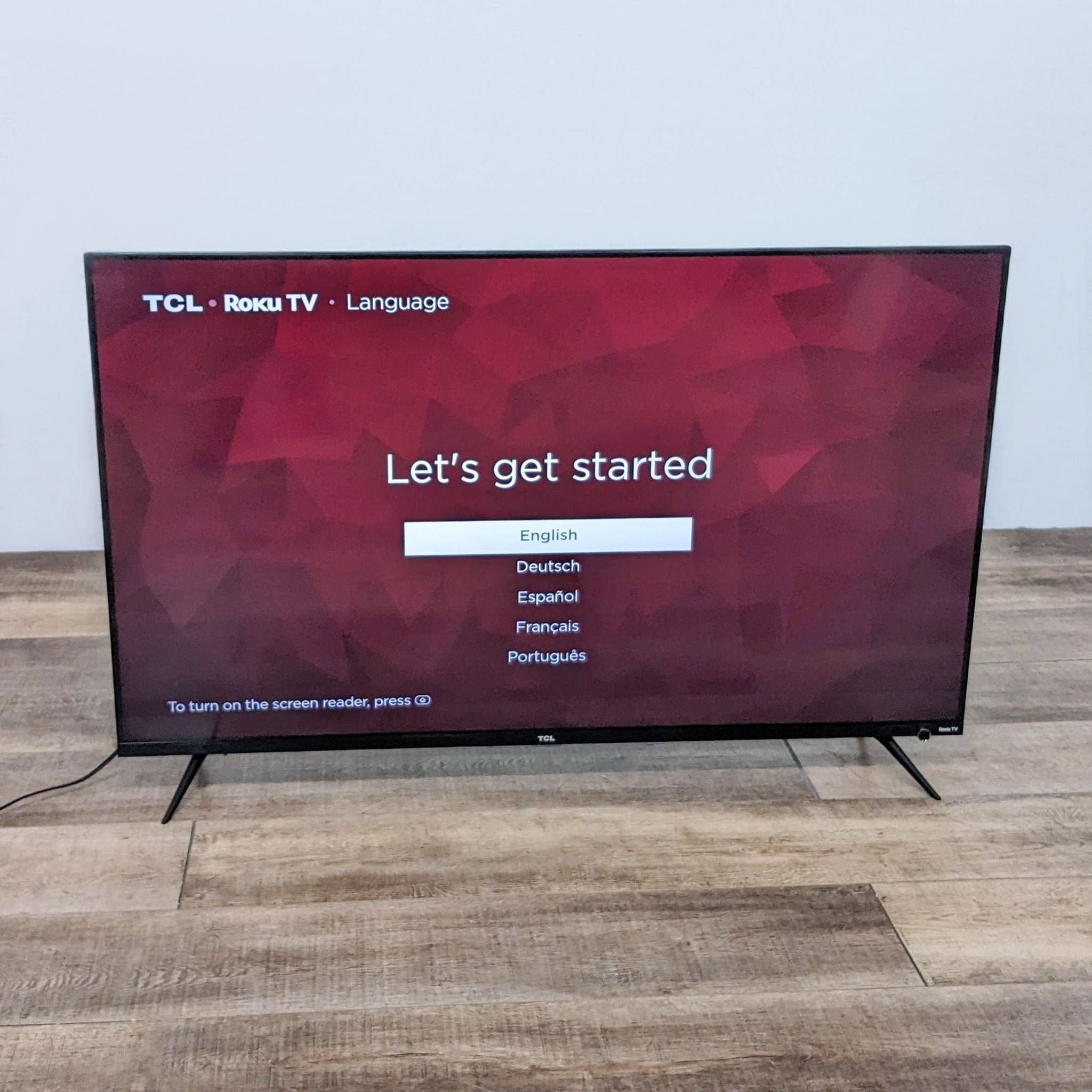 2. TCL 55S525 Roku TV powered on showing a "Let's get started" setup screen with language options, on a wooden floor.