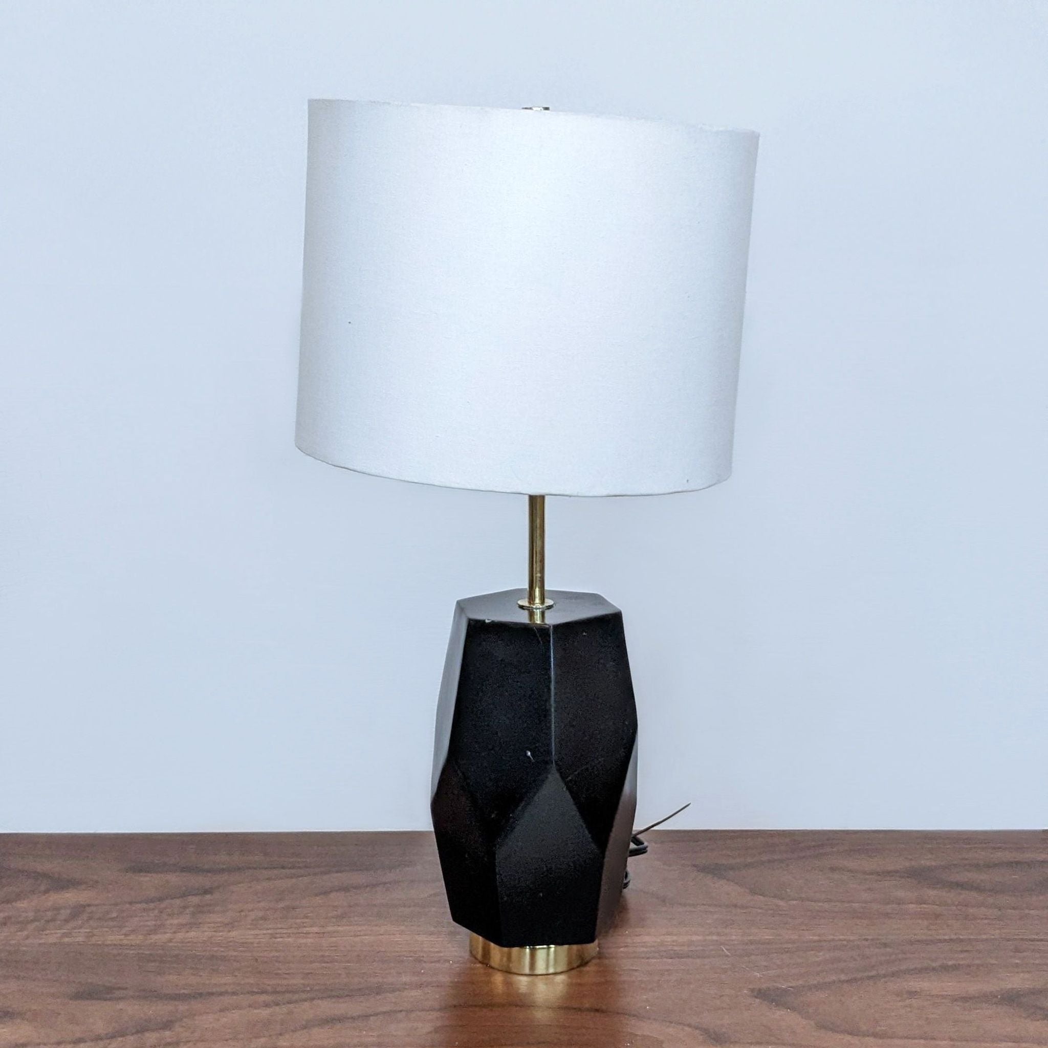 Reperch brand table lamp with a geometric black base and white shade on a wooden surface against a plain background.