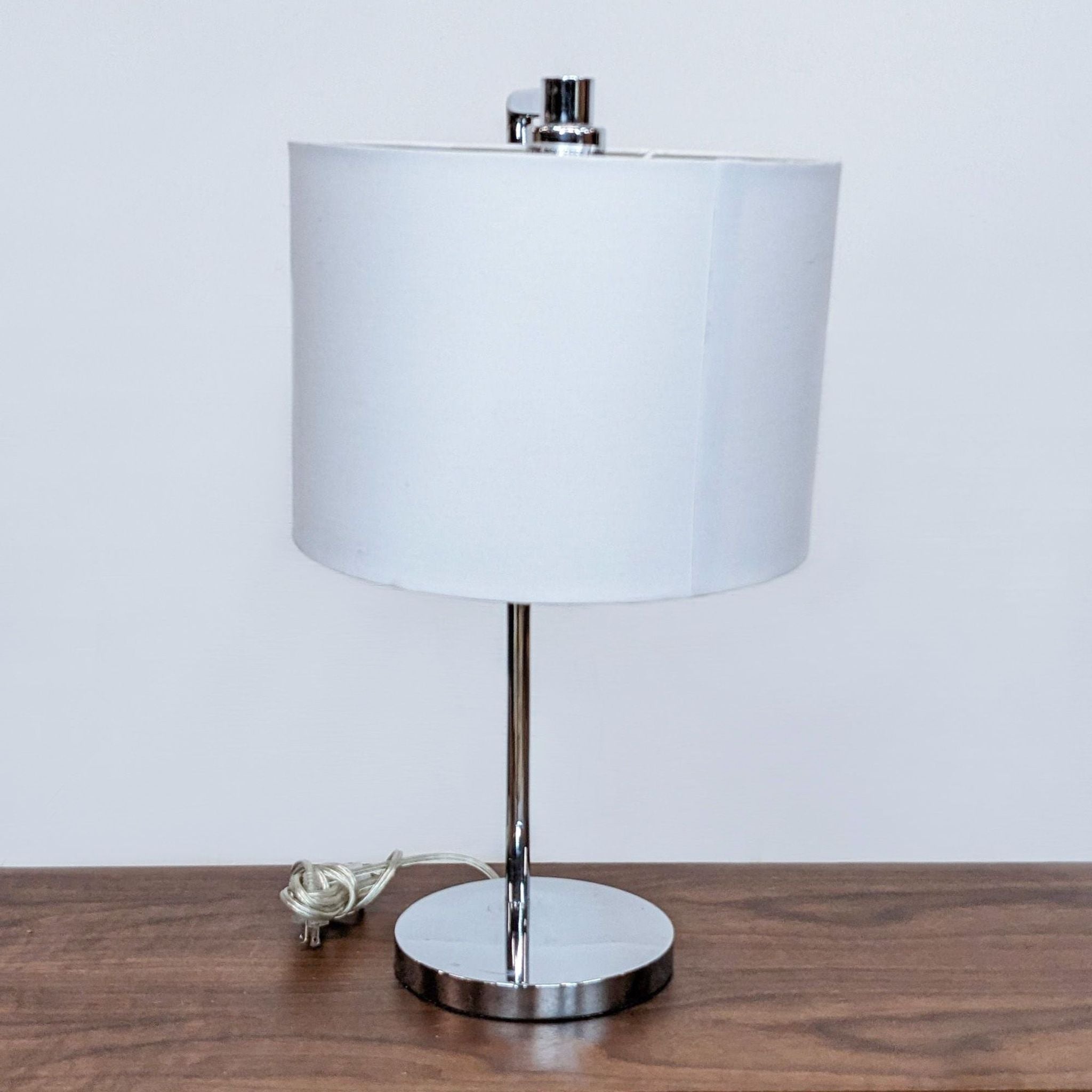 Minimalist Reperch desk lamp with a cylindrical white lampshade and shiny metal stand, power cord visible.