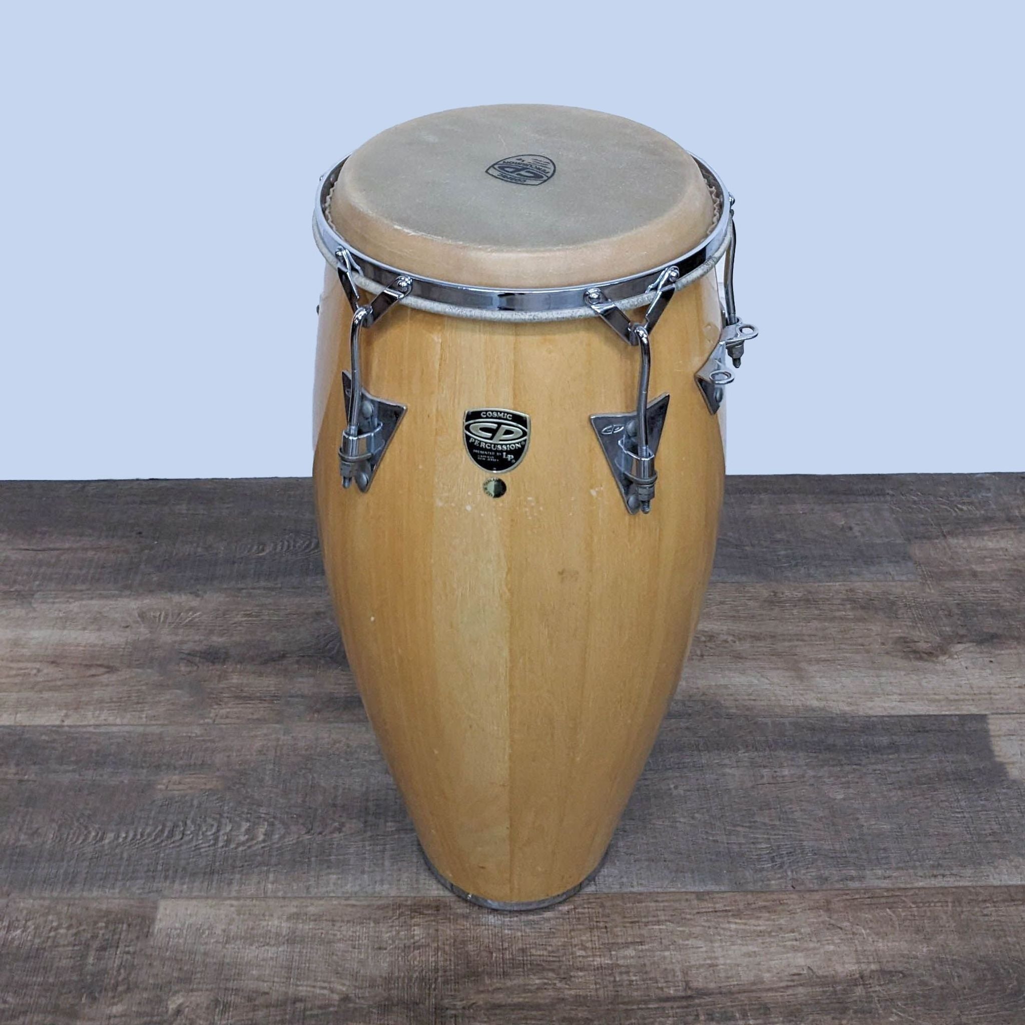 Alt text 1: A single Cosmic Percussion wooden conga drum with natural skin head and chrome hardware, stickered, against a wooden floor backdrop.