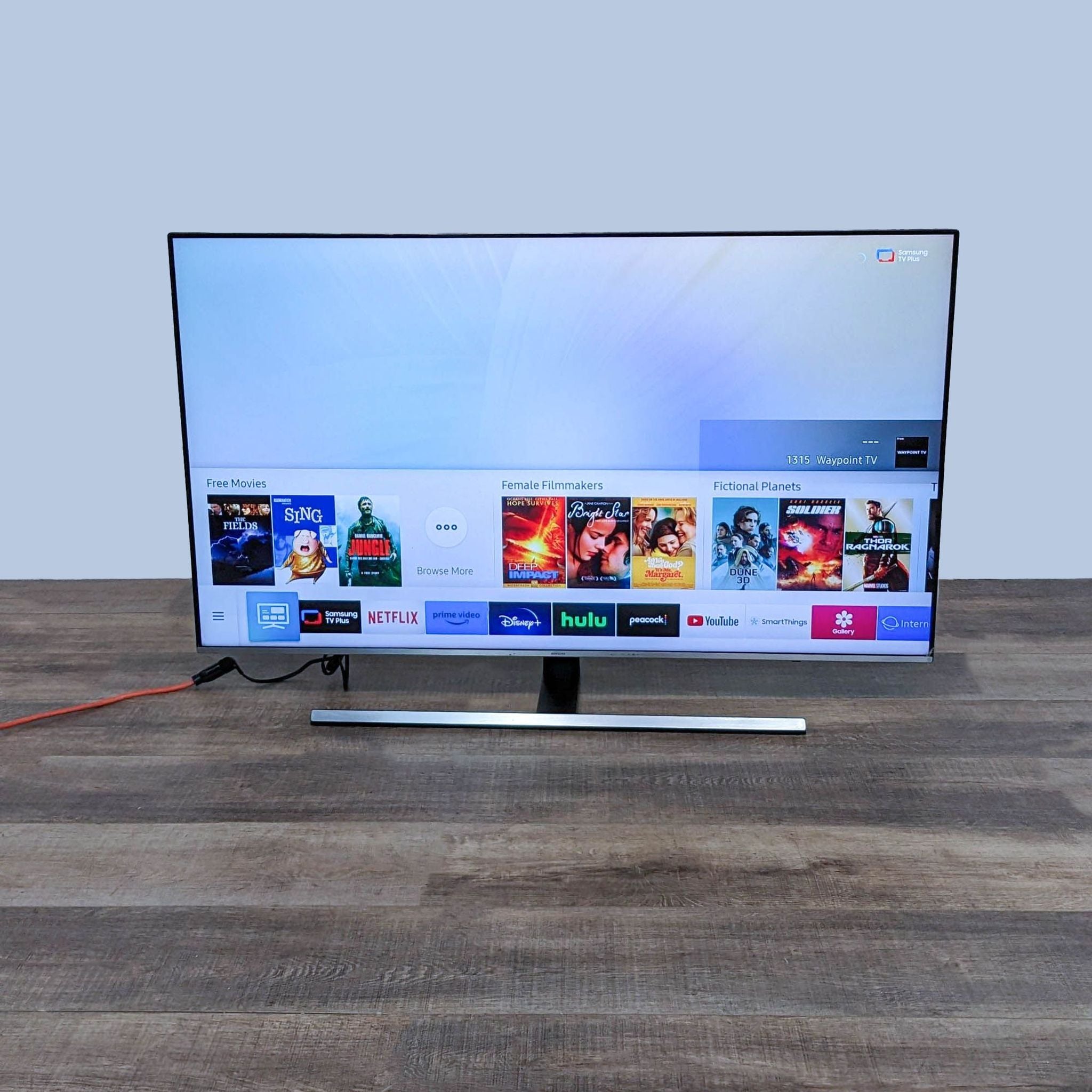 Samsung UN55NU8000F flat LED TV displaying smart interface with apps on screen, on a wooden surface.