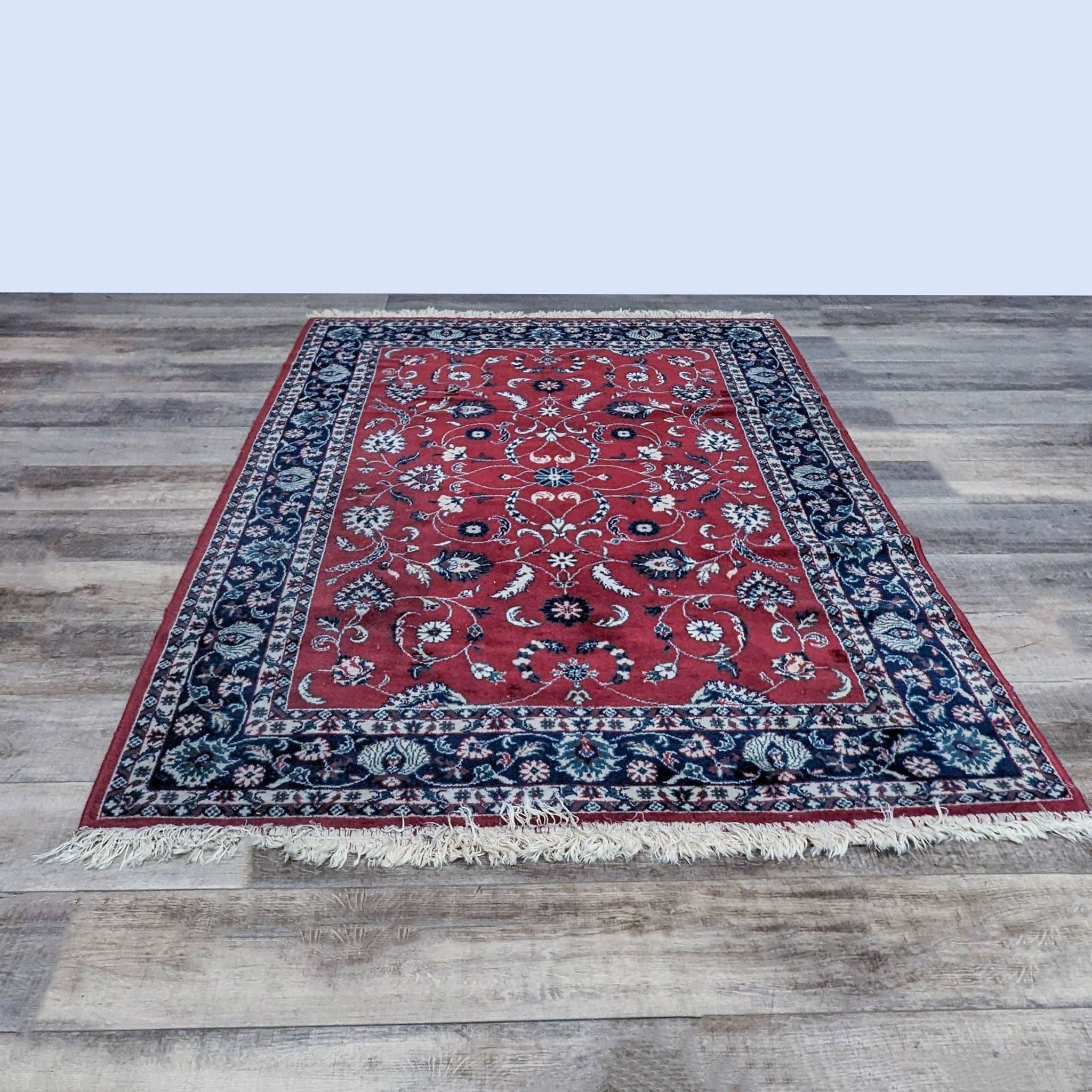 5' 7" x 8' 4" Reperch oriental wool area rug with red central field and intricate blue patterns, displayed on a wooden floor.