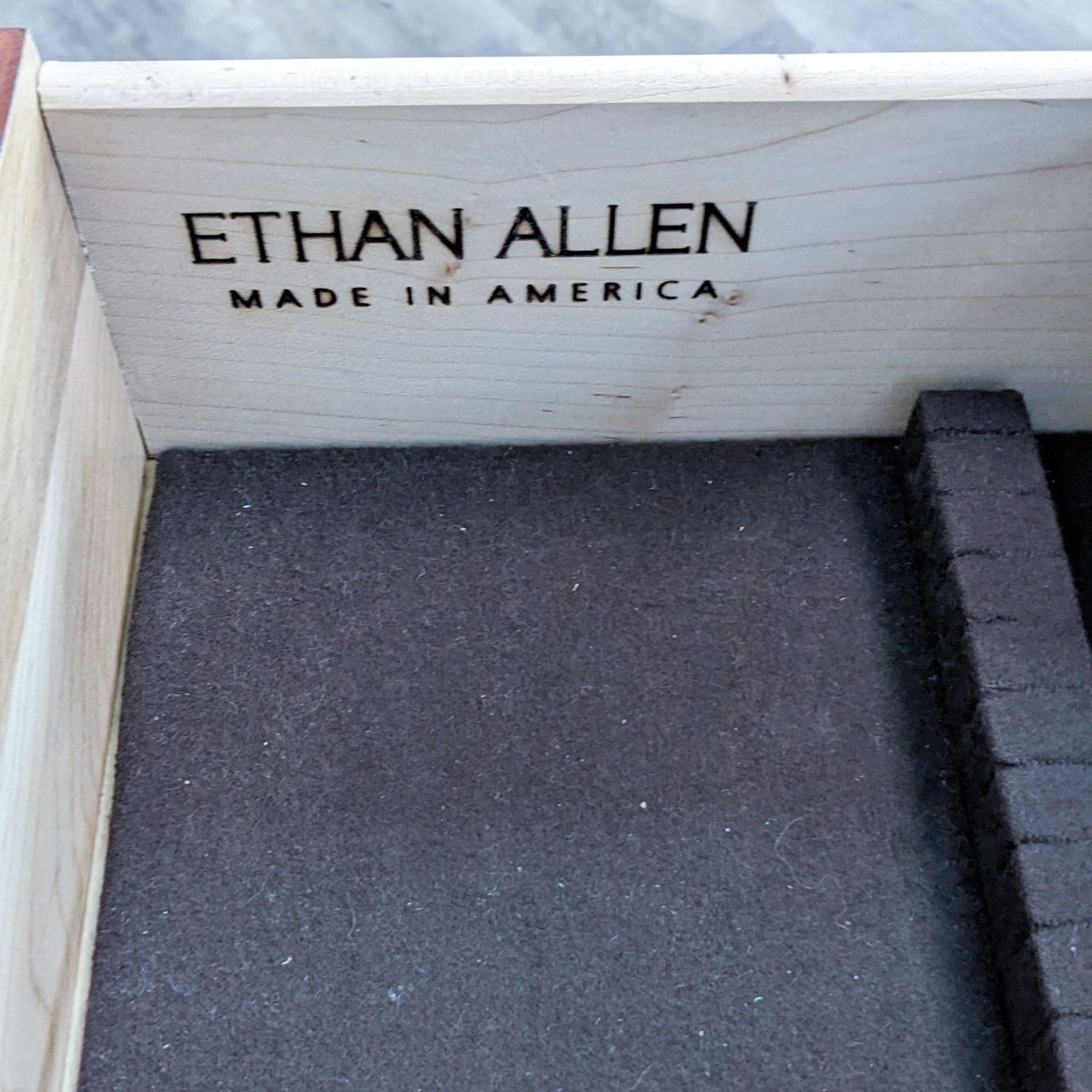 Close-up of Ethan Allen brand stamp inside a wooden drawer with gray lining.