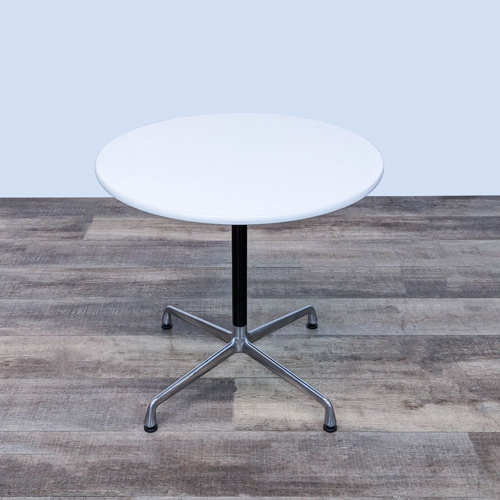 Modern Herman Miller Eames dining table, round white top, black and chrome base, depicted in an interior setting.