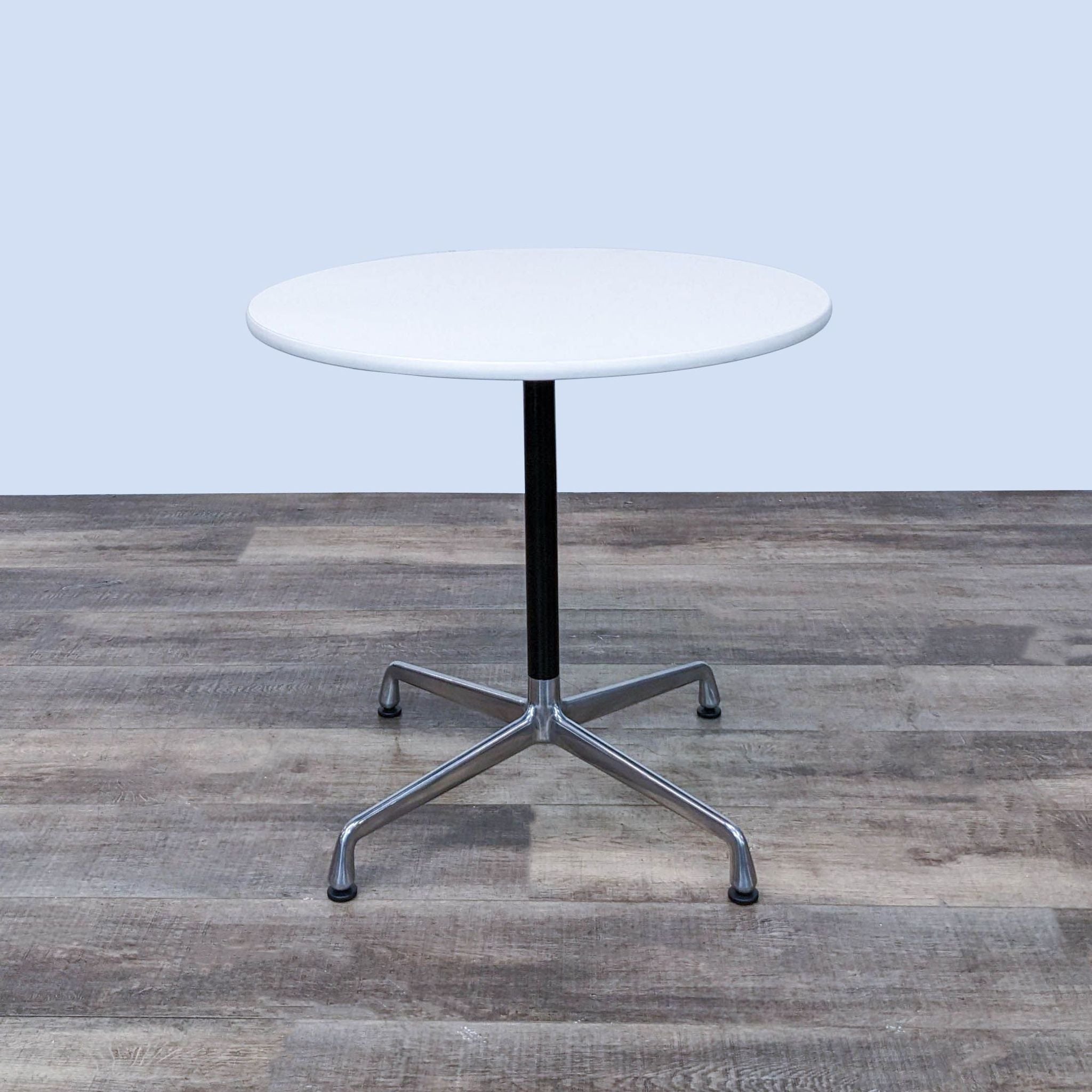 Herman Miller Eames modern round dining table with white top and chrome pedestal base on wood floor.