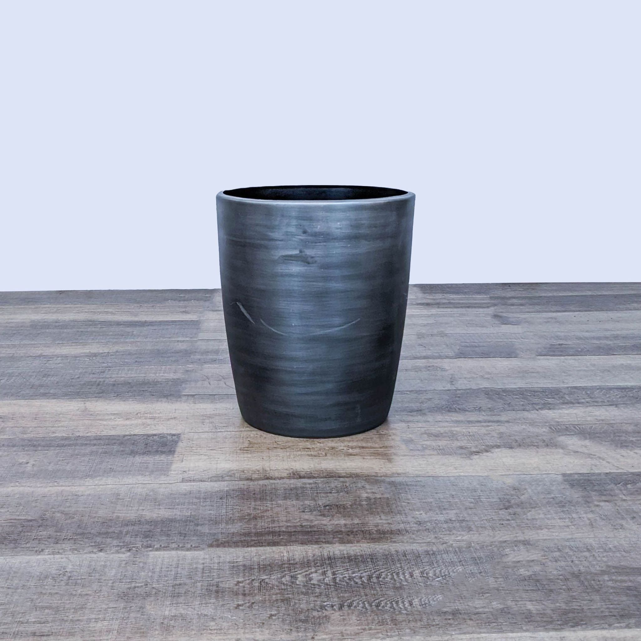 Reperch drum table on wooden floor, cylindrical shape with a black distressed finish.