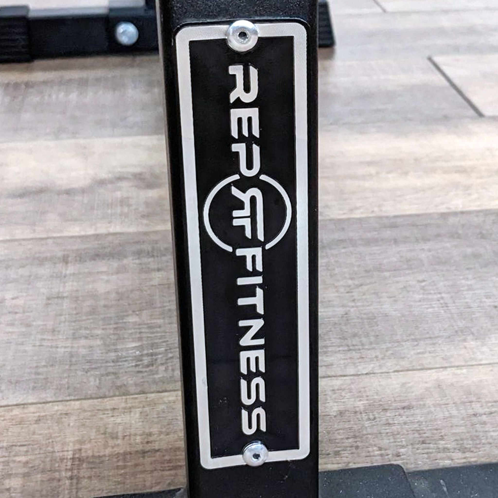 Close-up view of REP Fitness logo on the sturdy leg of a solid steel flat bench for supportive exercises. 