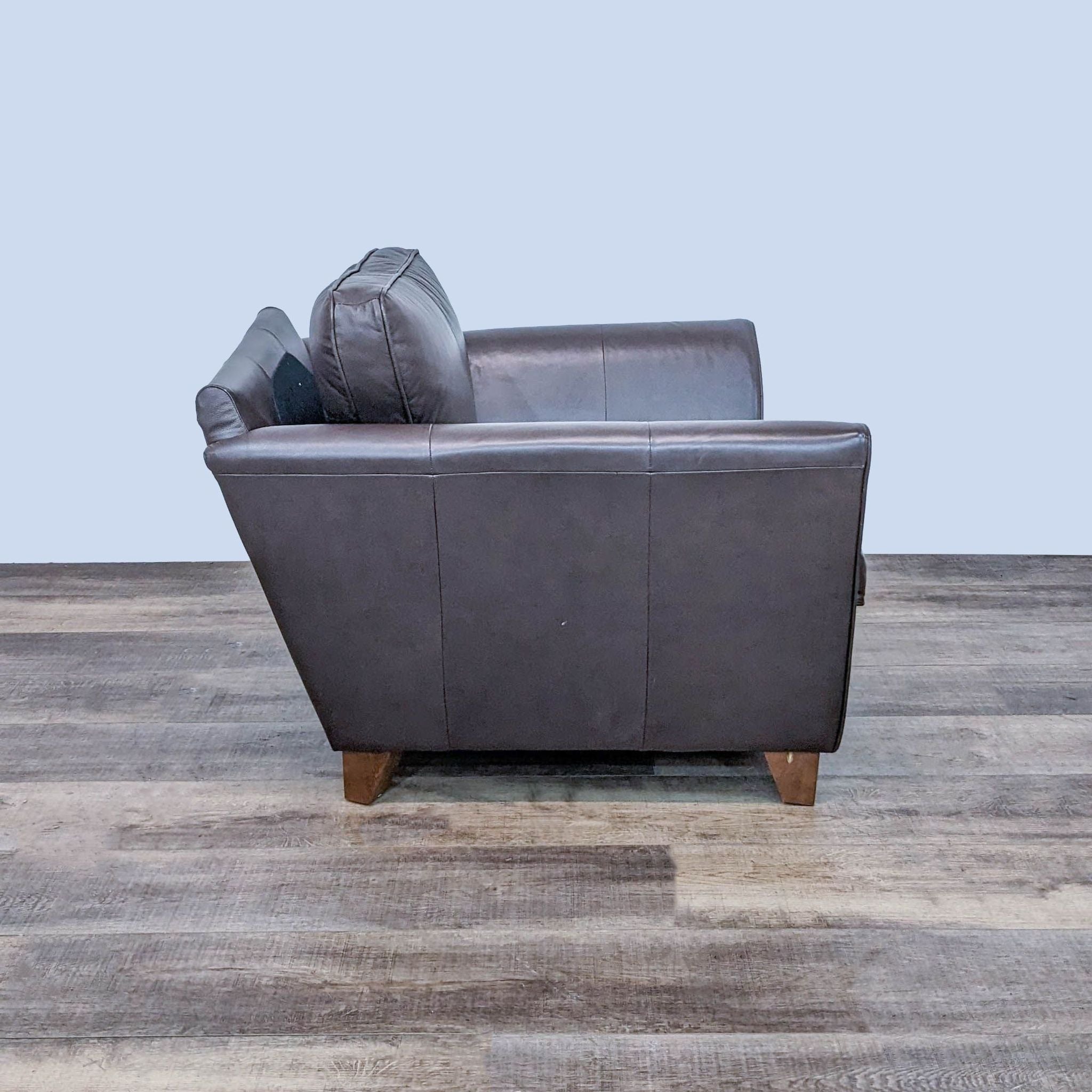 Rear view of a Marks & Spencer dark leather chair with tapered wooden legs, showing the armchair’s high back and side contours.
