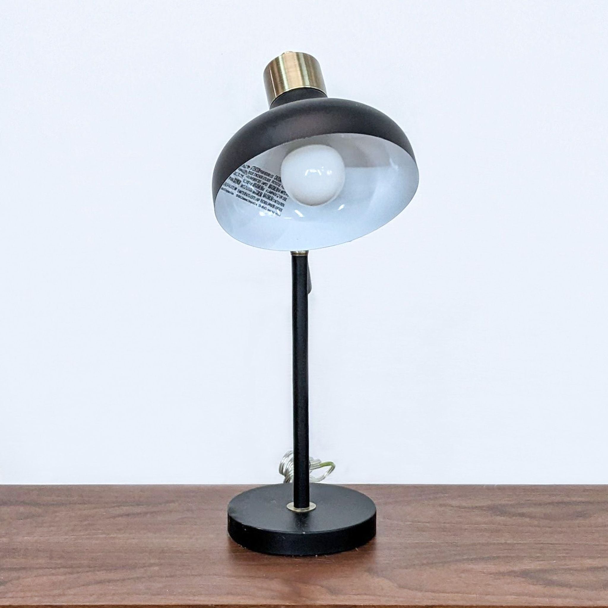Elegant Reperch desk light featuring brass fixtures and a translucent glass bulb cover, displayed on a wooden surface.