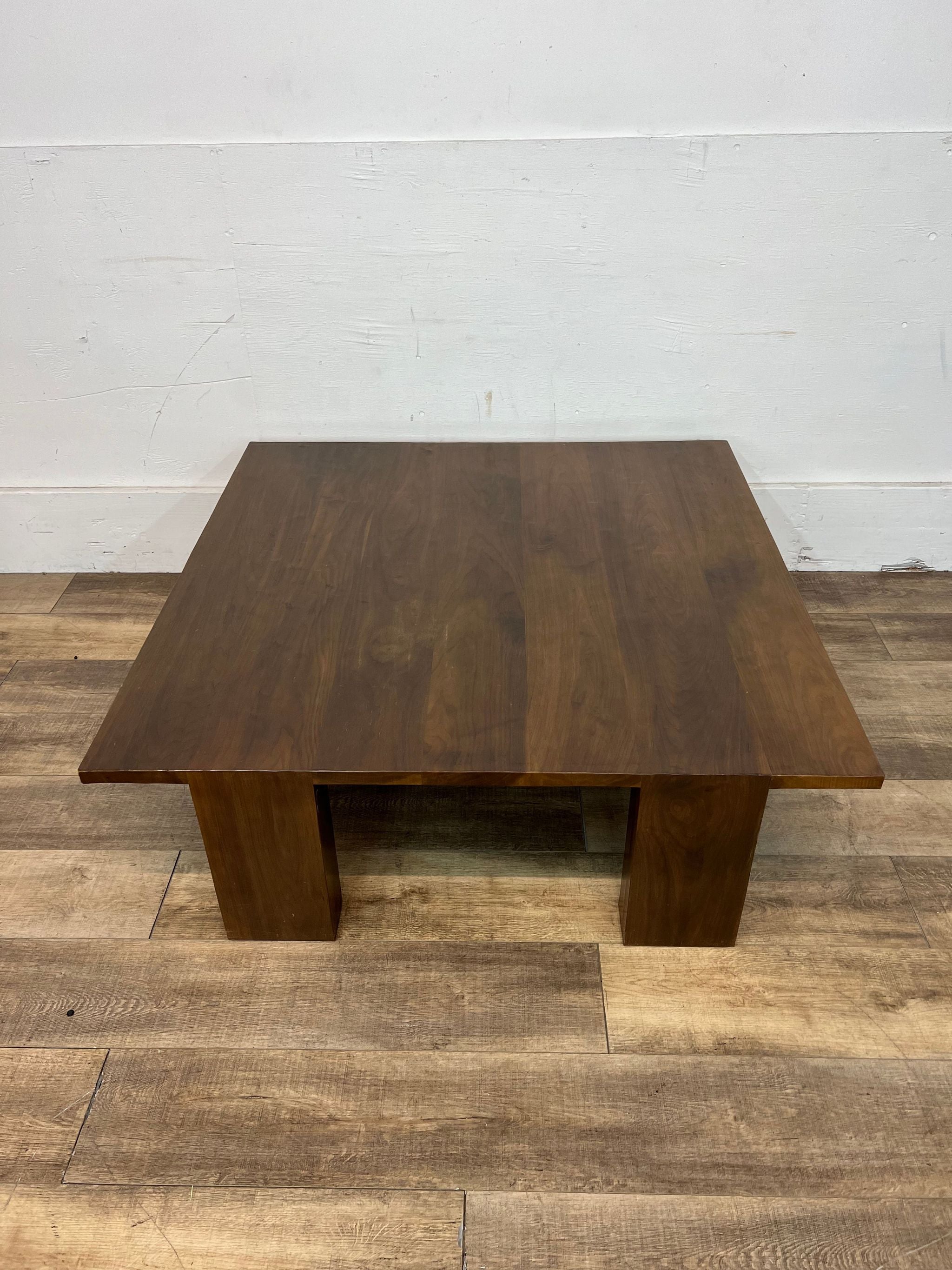 Kendall Wilkinson Design Workshop custom hewn walnut coffee table against a white wall on wooden flooring.