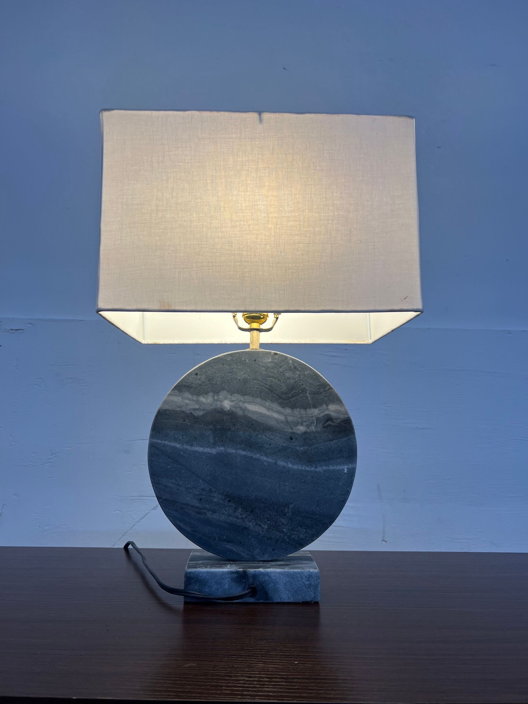 Illuminated Reperch brand table lamp with a fabric shade and round polished marble base on a wooden surface.