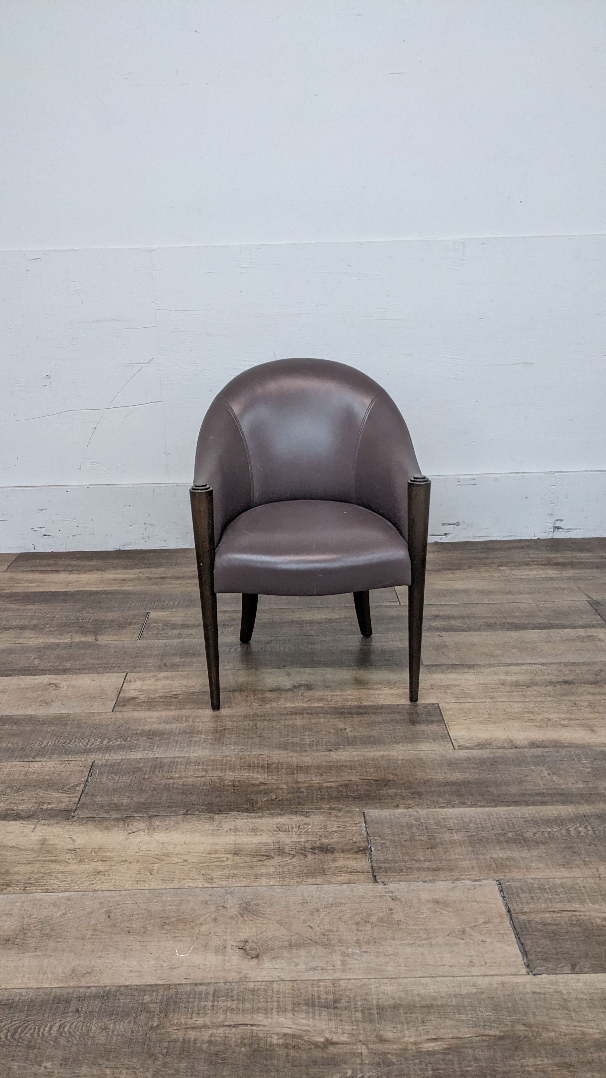 Donghia leather tub back chair with rounded back and tapered legs, on a wooden floor against a white wall.