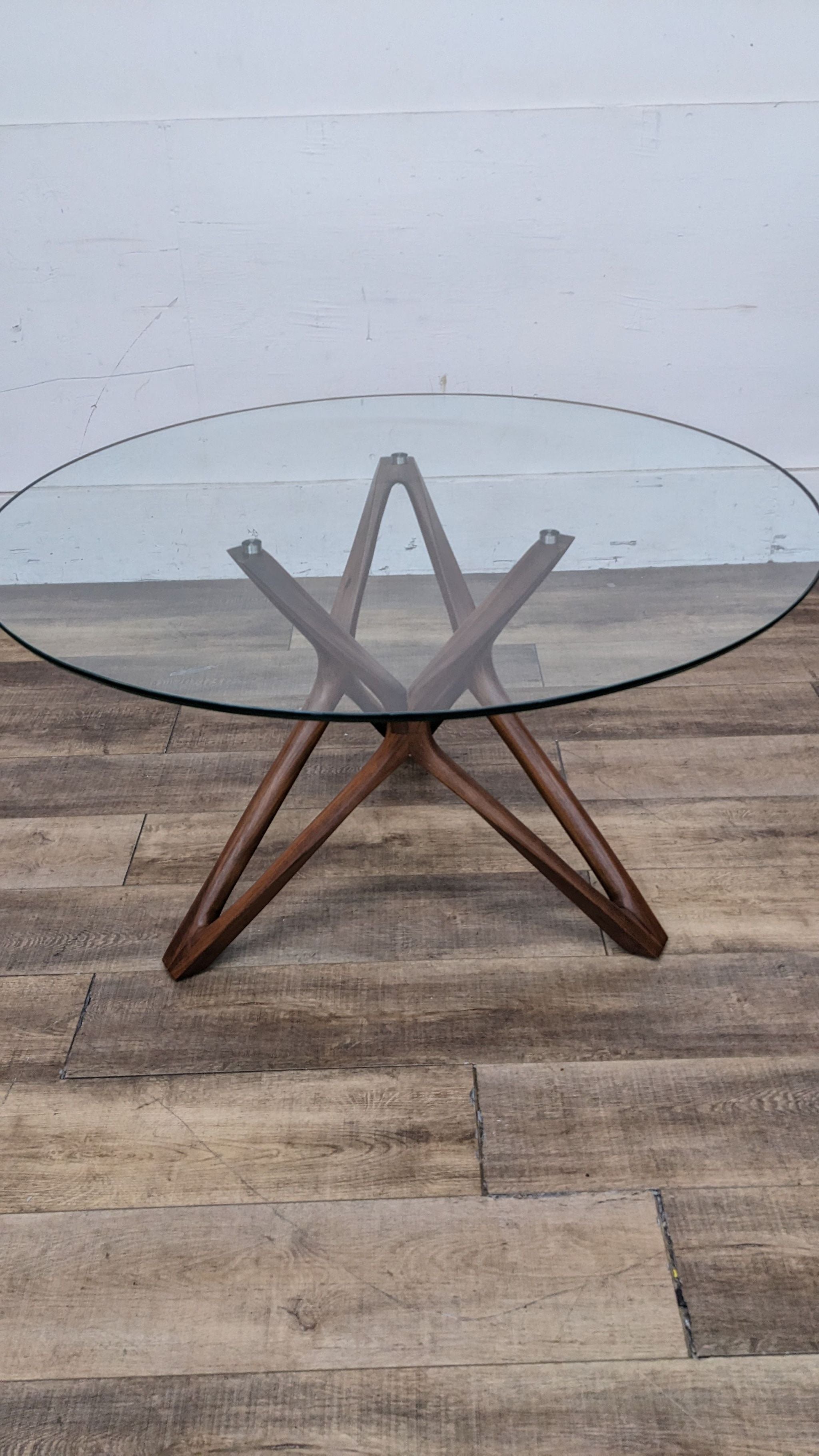Elegant dining table by Scandinavian Design with a transparent round top and intersecting wooden legs for a modern, airy dining space.