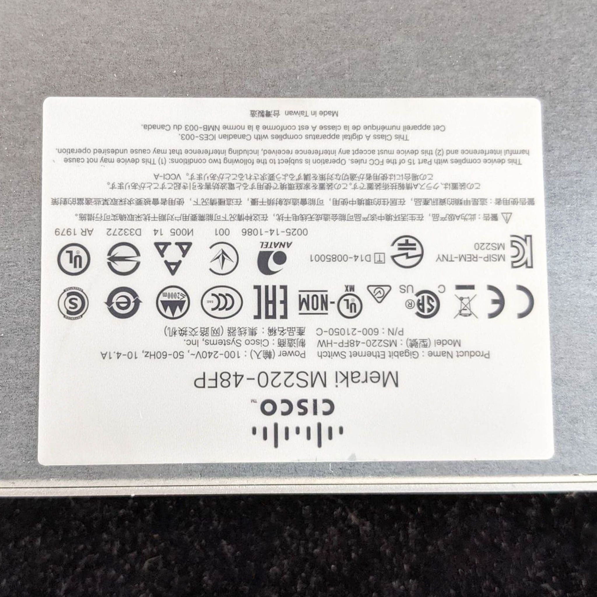 Label on the bottom of a Cisco networking device displaying model information and regulatory icons.