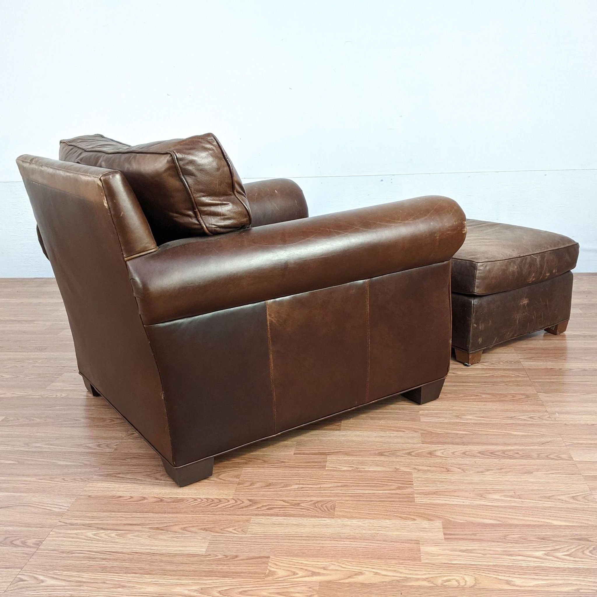 A Pottery Barn brown leather club chair with matching ottoman on a hardwood floor, belonging to lounge category.