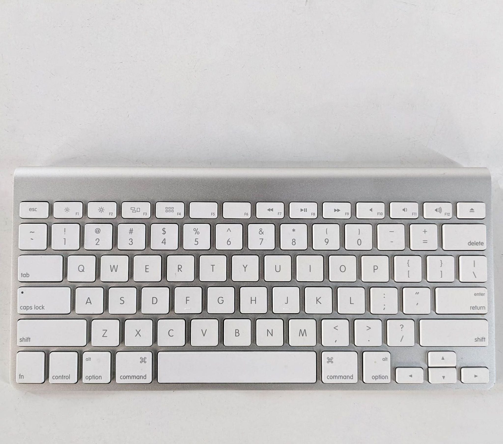Alt text 1: Apple brand wireless keyboard on white surface, showing a clean design with grey and white keys.